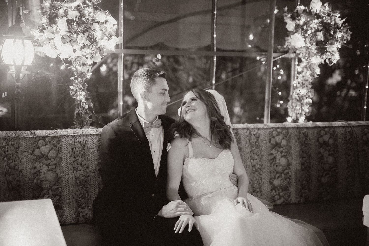 Romantic couple shares a candid moment under twinkling lights and floral decor at their wedding reception.