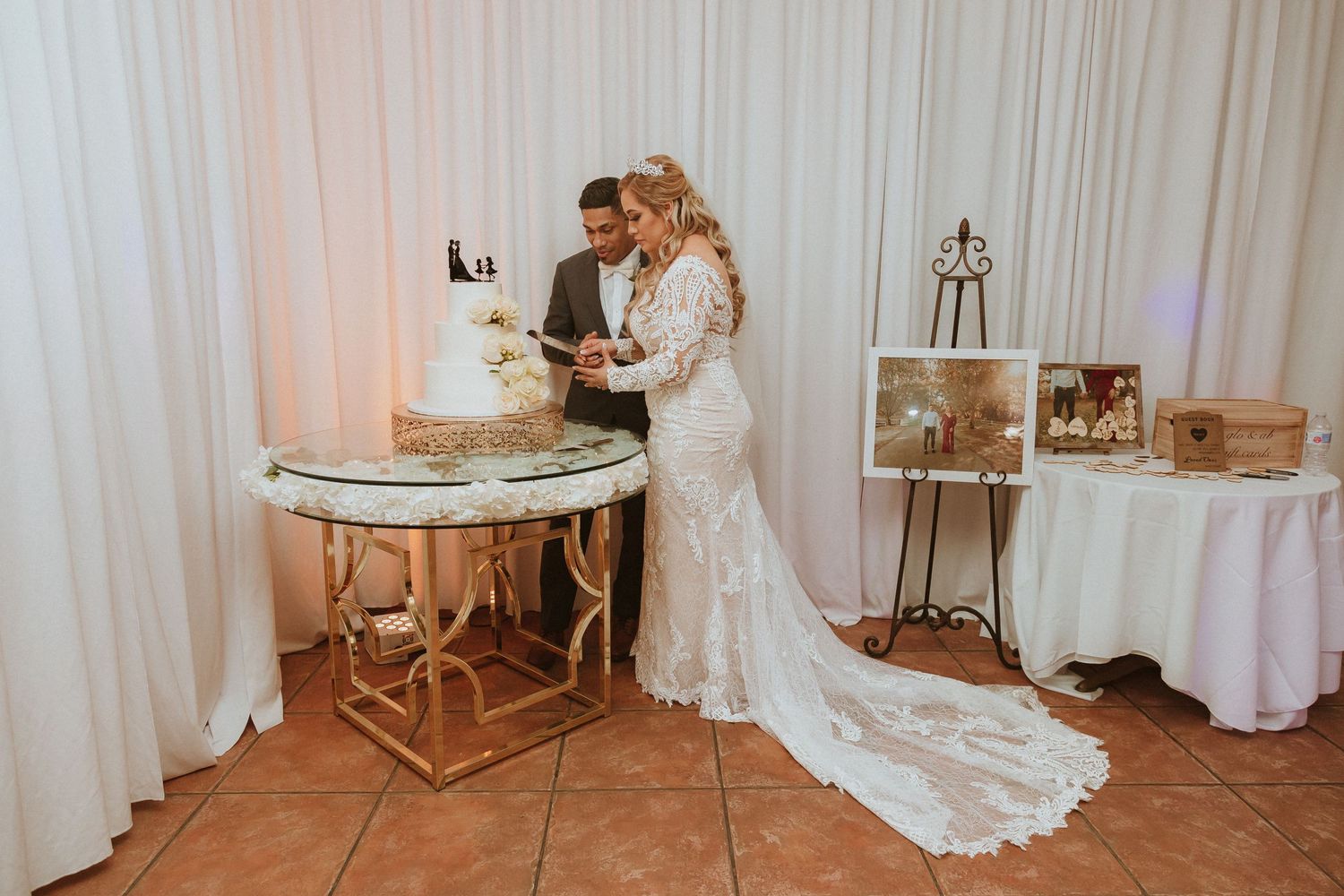 Newlyweds cutting their wedding cake at elegant reception with white backdrop.