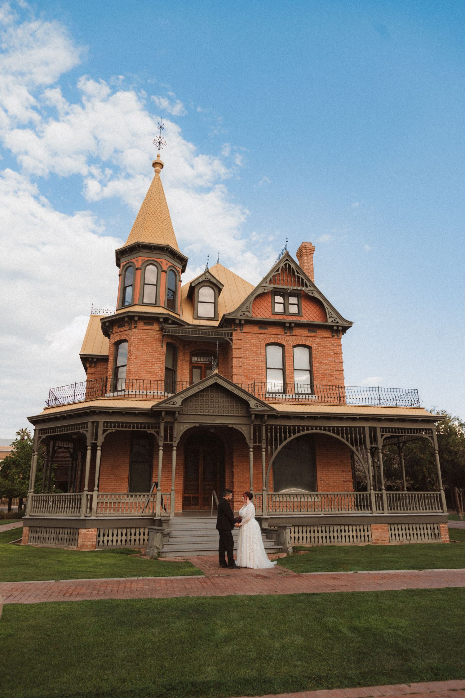 An elegant wedding photo featuring a stunning Victorian-era mansion with tower and wraparound porch.