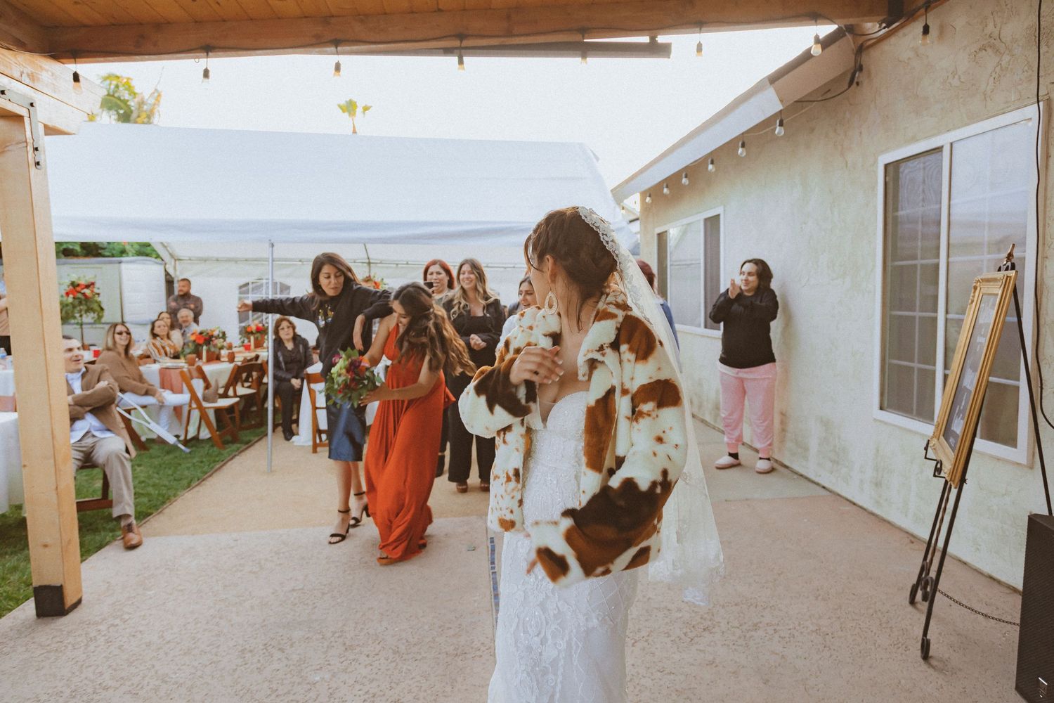 A bride in a lace gown prepares to toss her bouquet at an outdoor wedding reception.