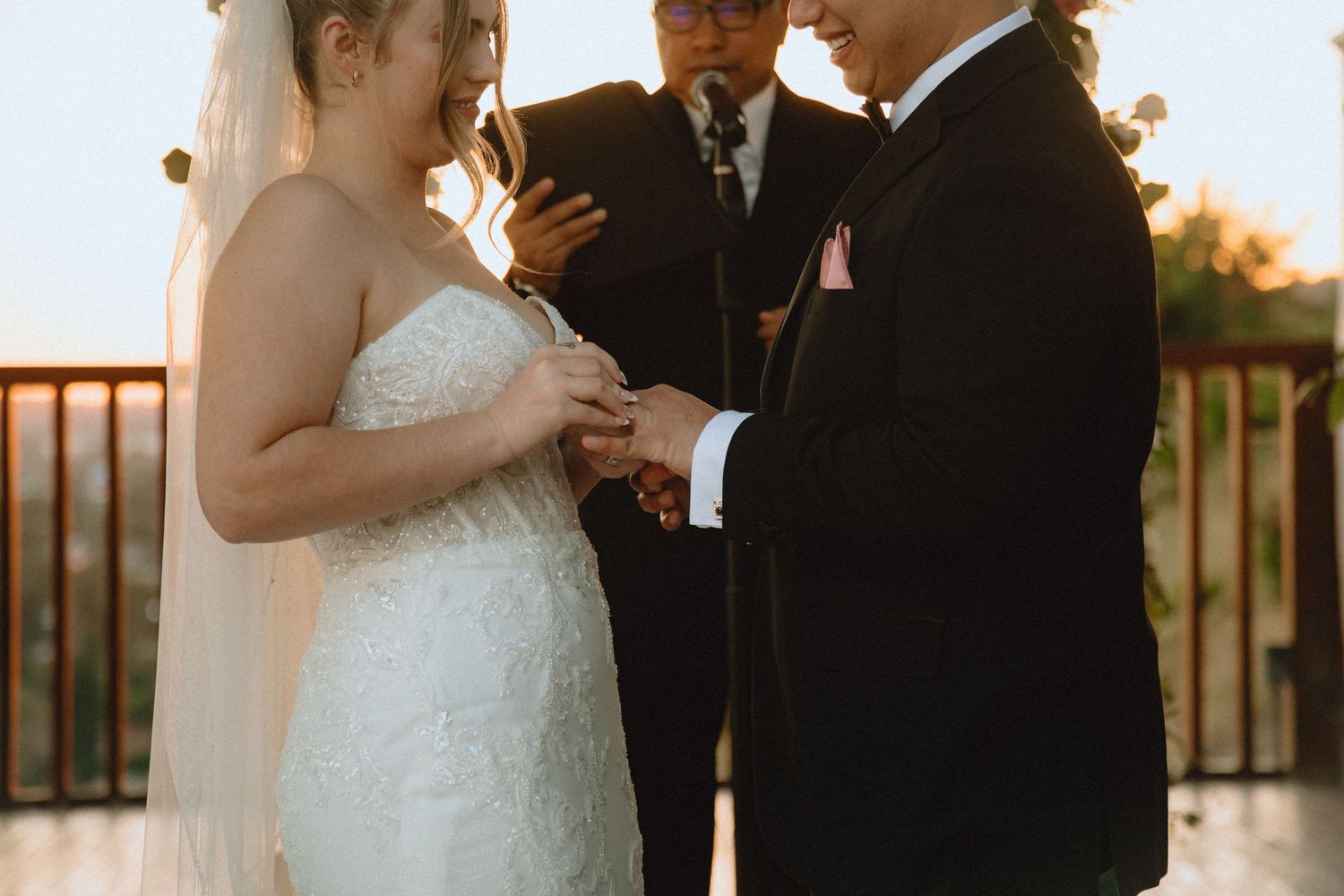 A couple exchanges rings during their sunset wedding ceremony under a decorated outdoor arbor.