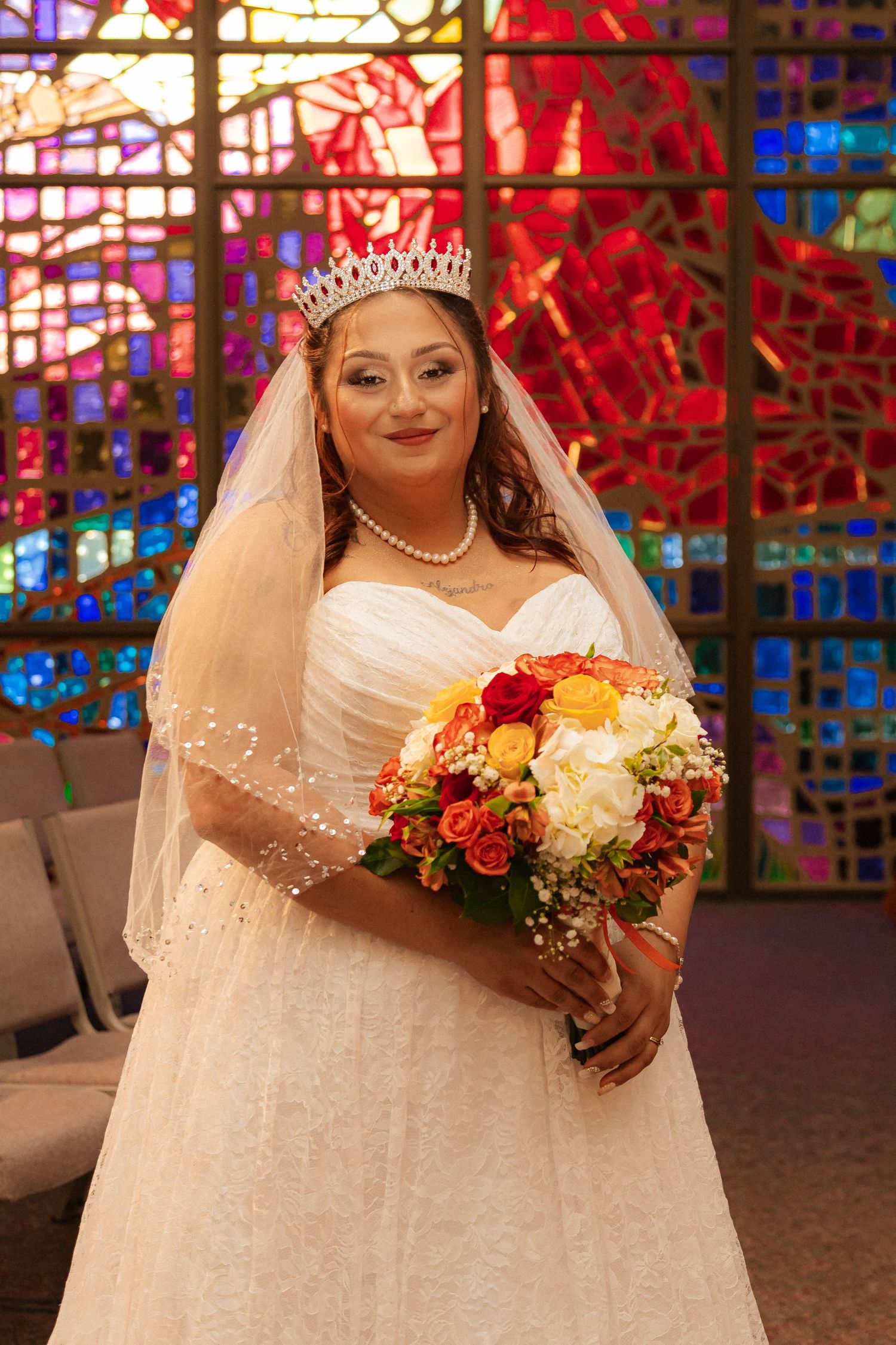 Bride holds autumn-colored bouquet while posing in front of dramatic stained glass church windows.