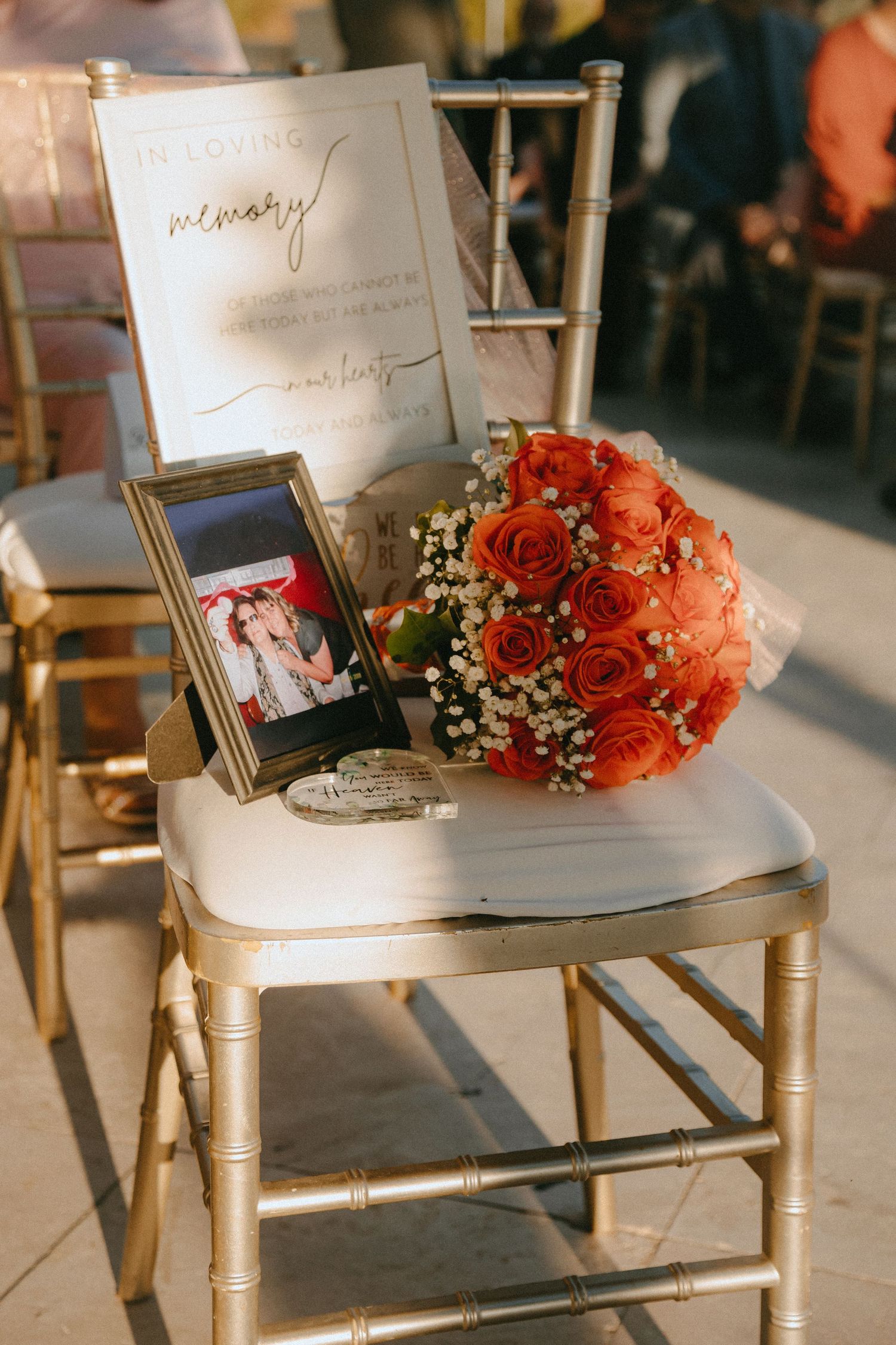 Wedding reception detail of coral rose bouquet and framed photo arranged on gold chair.