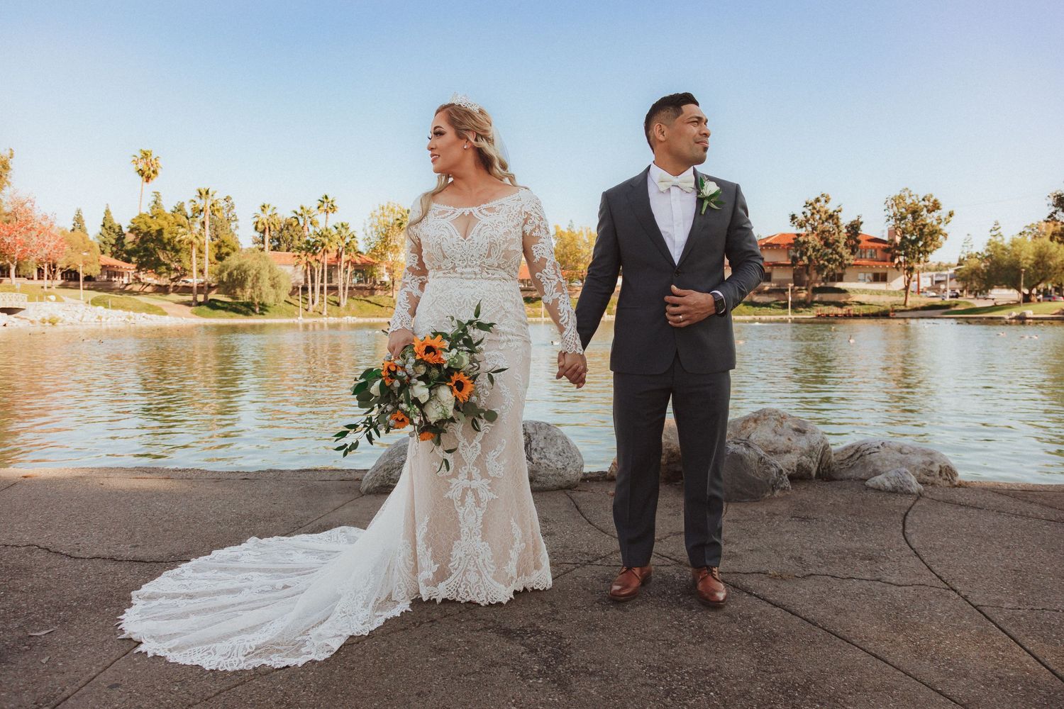 Full length wedding portrait of couple walking by tranquil lake.