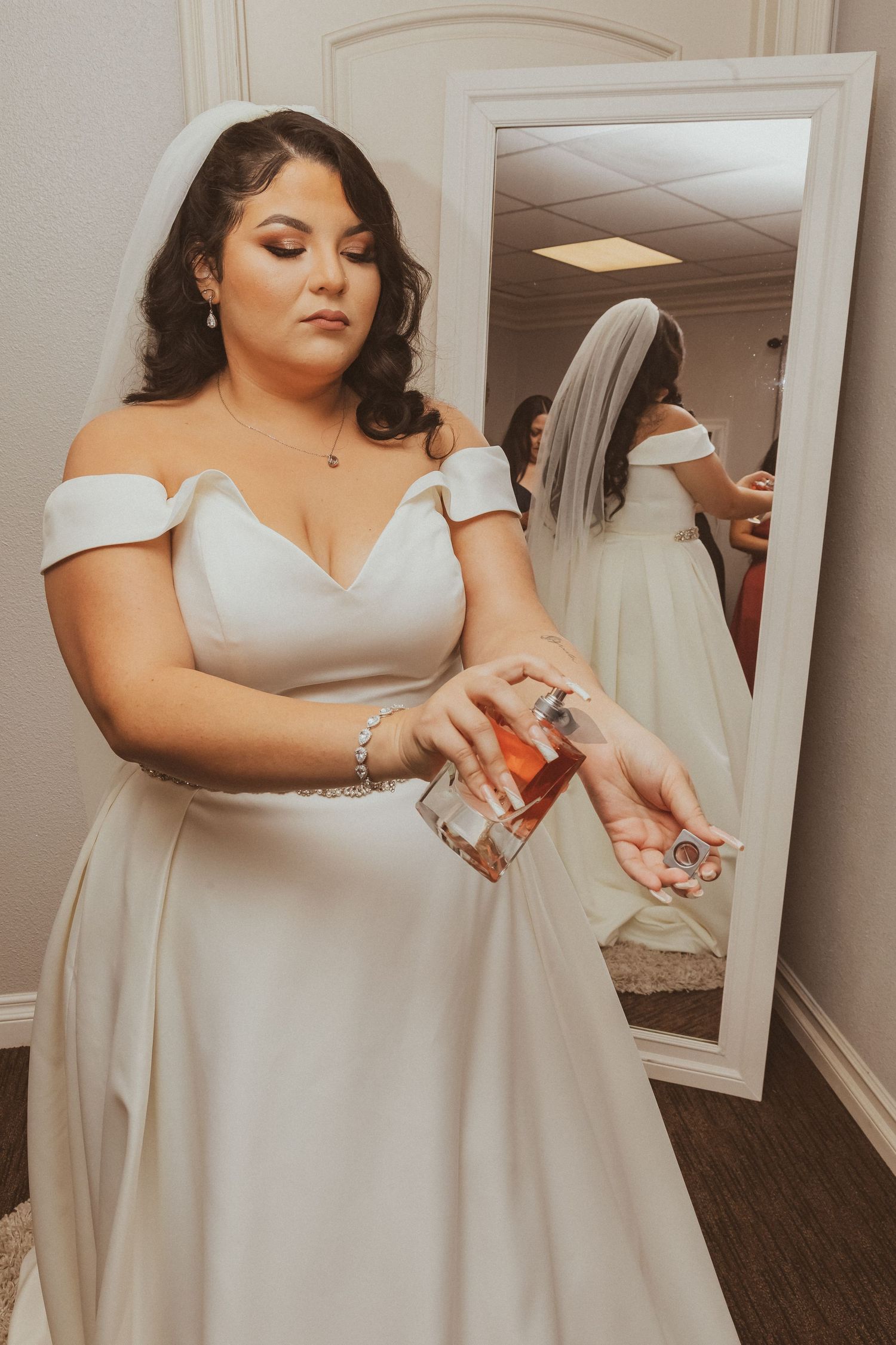Wedding dress detail featuring an off-shoulder neckline and flowing skirt in a dressing room setting.