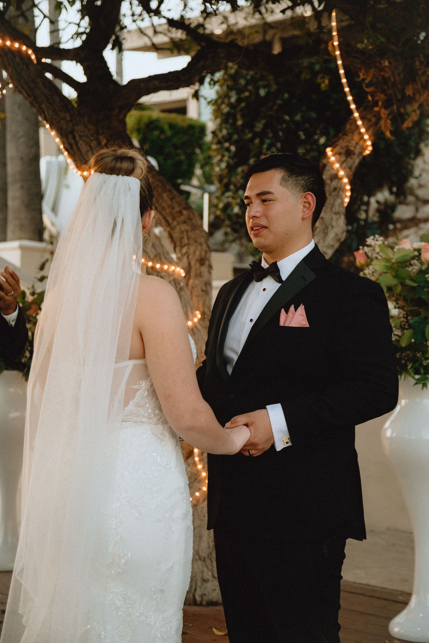 Wedding couple exchanges vows at outdoor ceremony with fairy lights and natural decor.