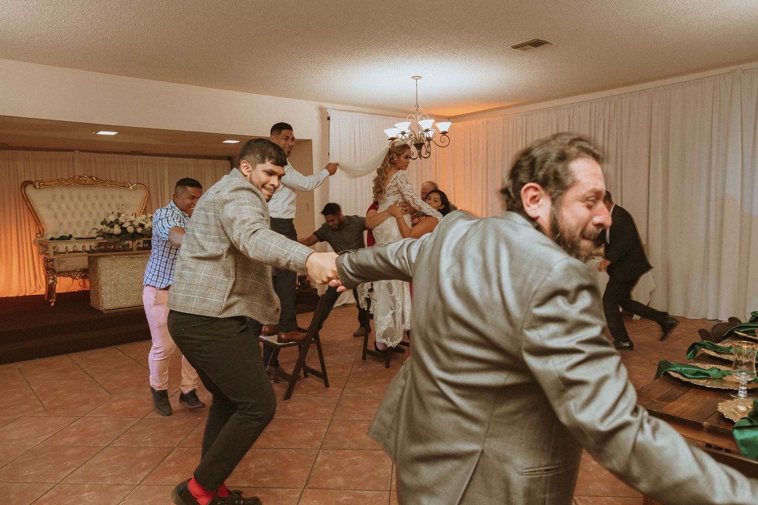 People dancing enthusiastically at an indoor party with chairs and decorations visible.