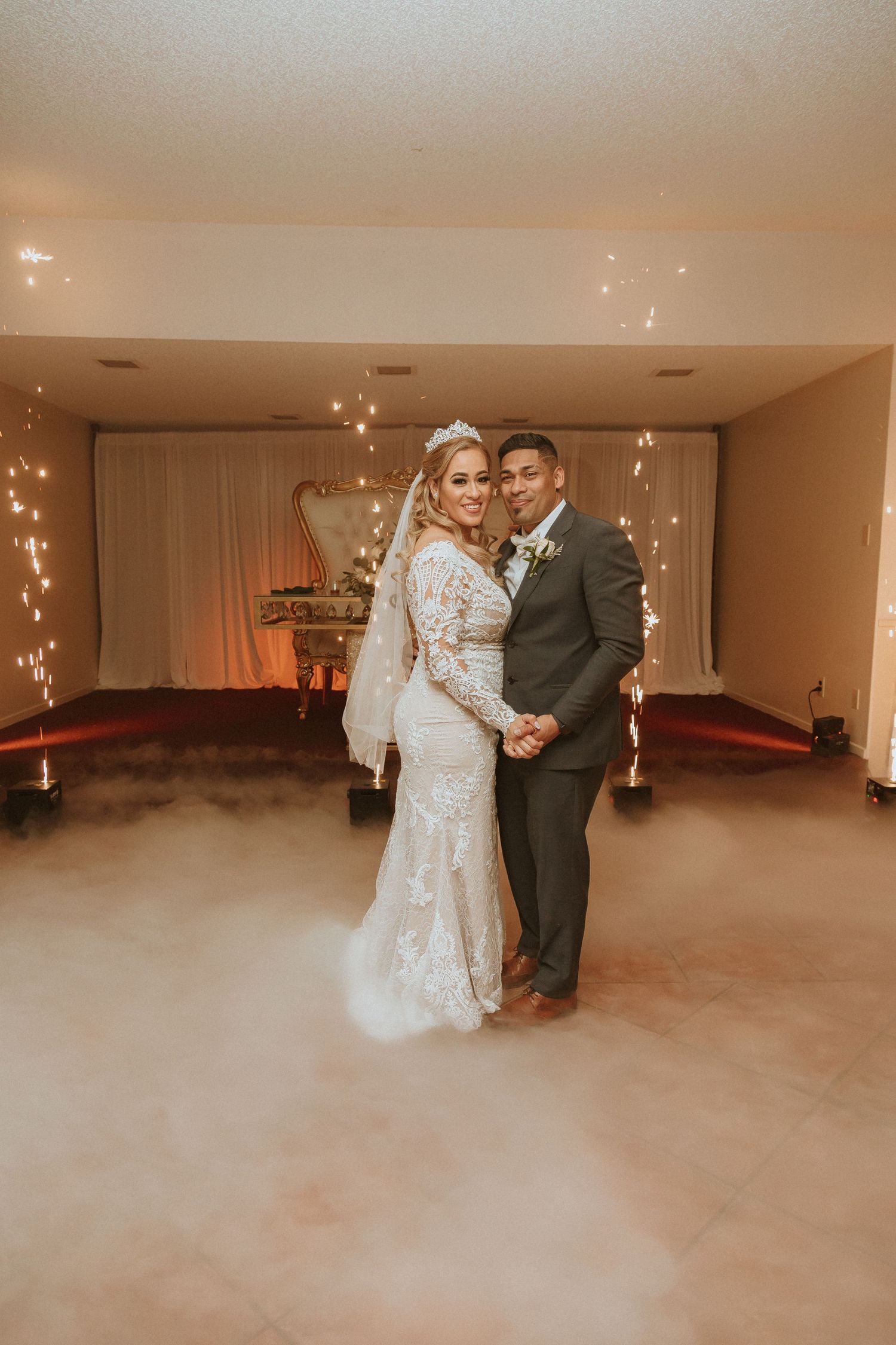 A wedding photo showing the couple against white drapes with fog effects and sparkler fountains.