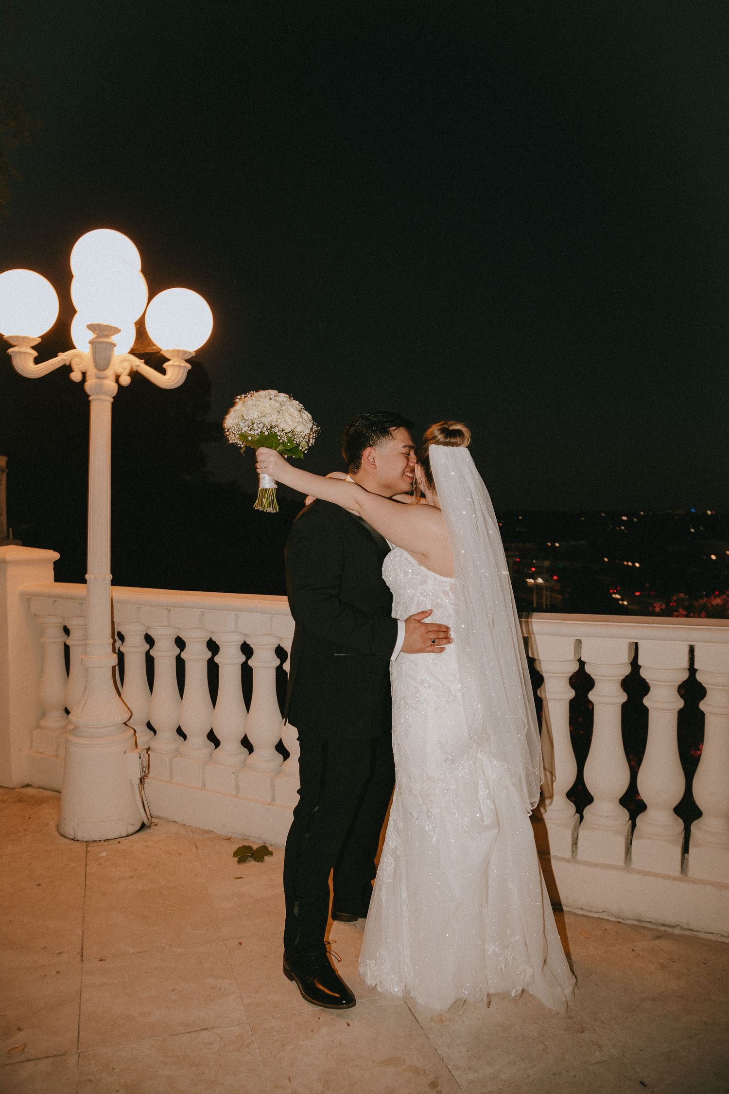 A wedding couple dances and celebrates on an elegant balcony with vintage lighting.