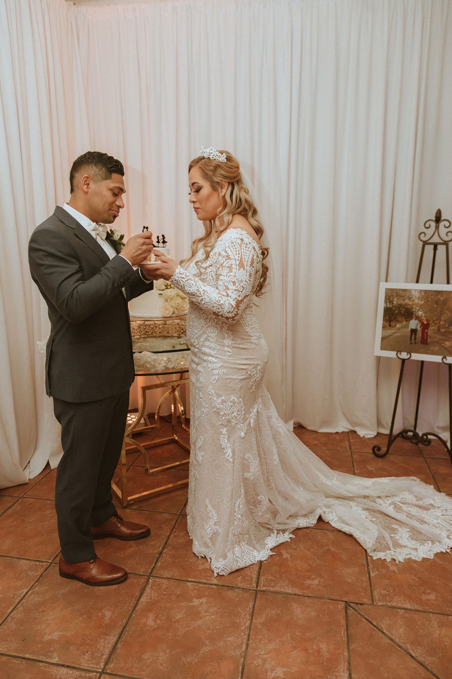 Wedding couple enjoying cake-feeding tradition in front of decorative backdrop.