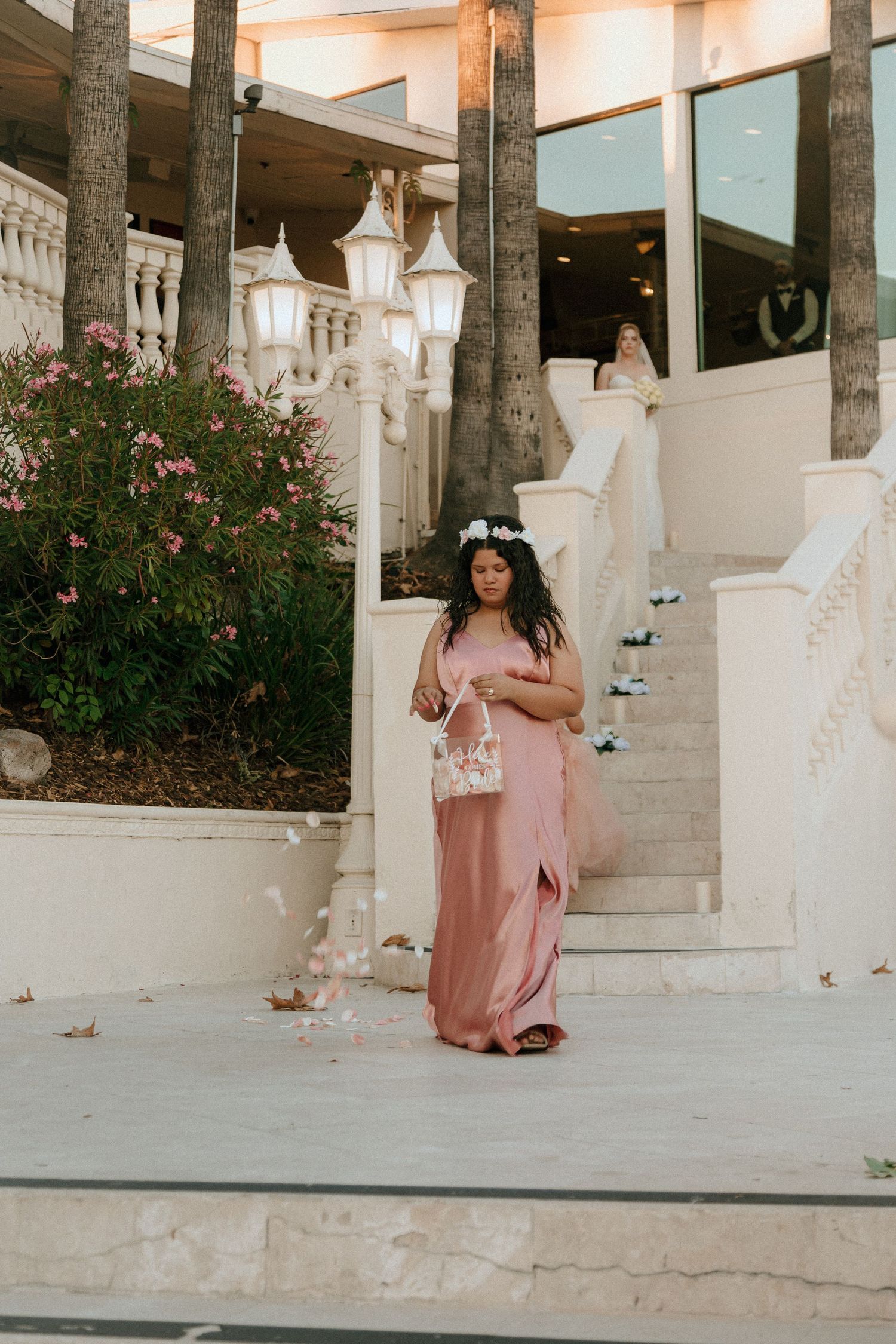 Person in flowing pink dress poses on elegant white staircase with lanterns and palm trees.