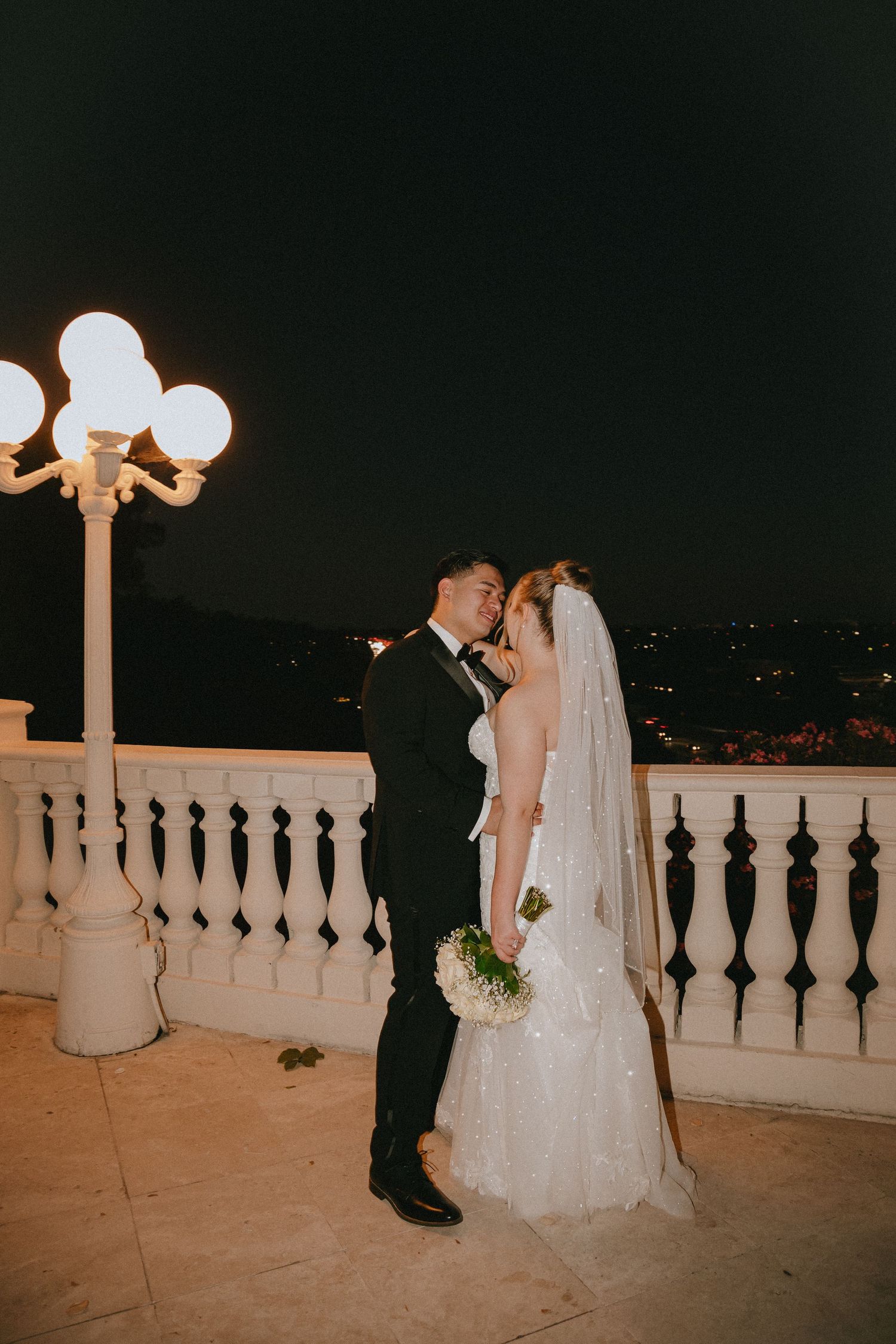 Elegant wedding portrait taken at night on a balcony with glowing lampposts.