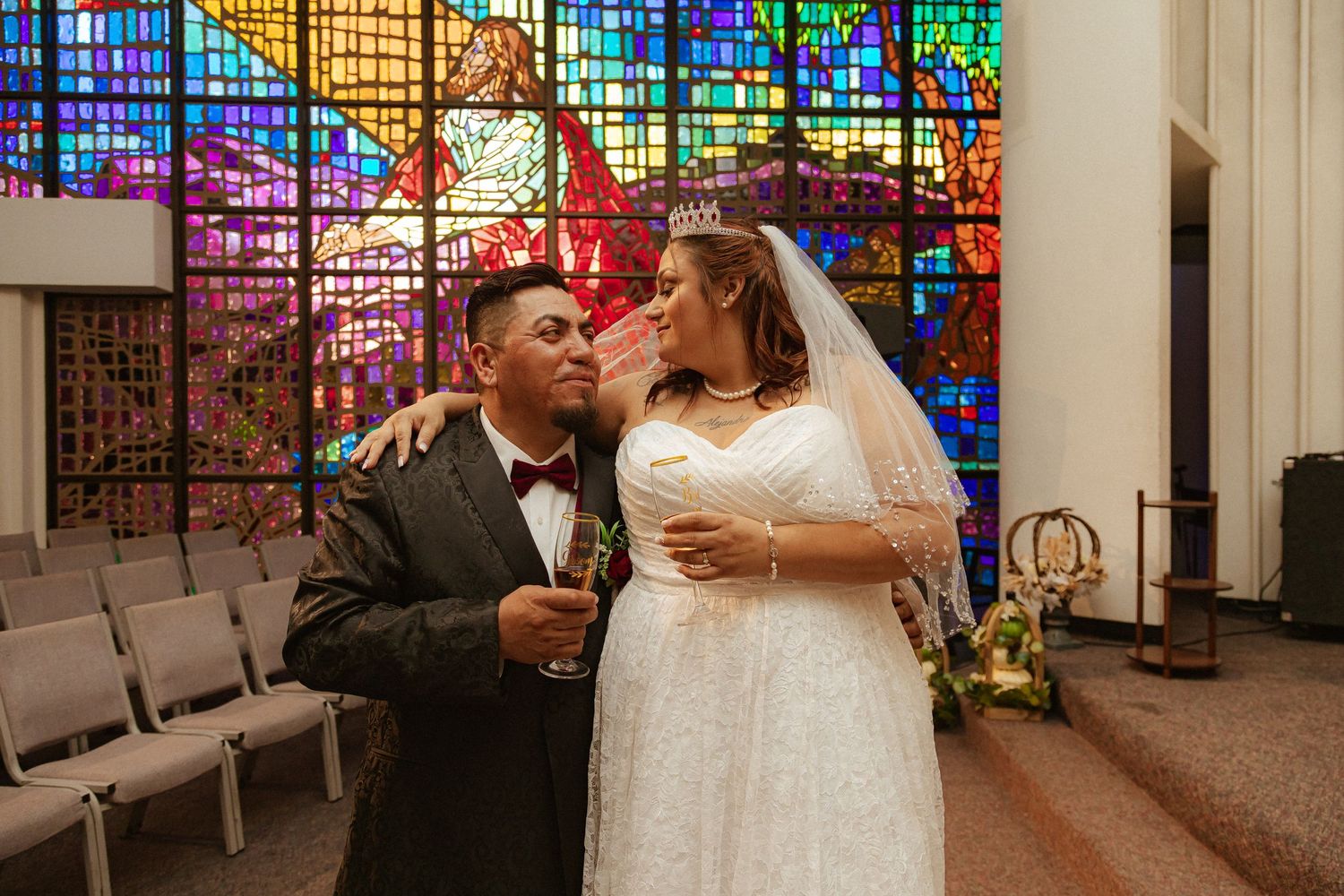 A joyful moment between newlyweds in front of colorful church stained glass windows.
