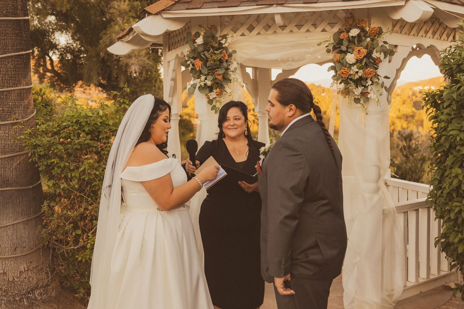 Sunset wedding ceremony under decorated gazebo with palm trees and floral arrangements.