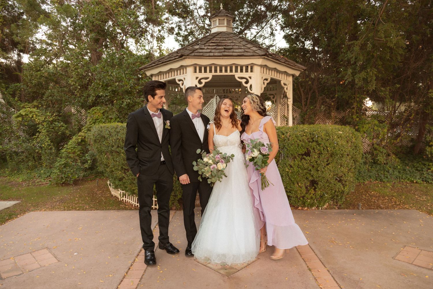 Wedding party standing together in front of a wooden gazebo during golden hour.