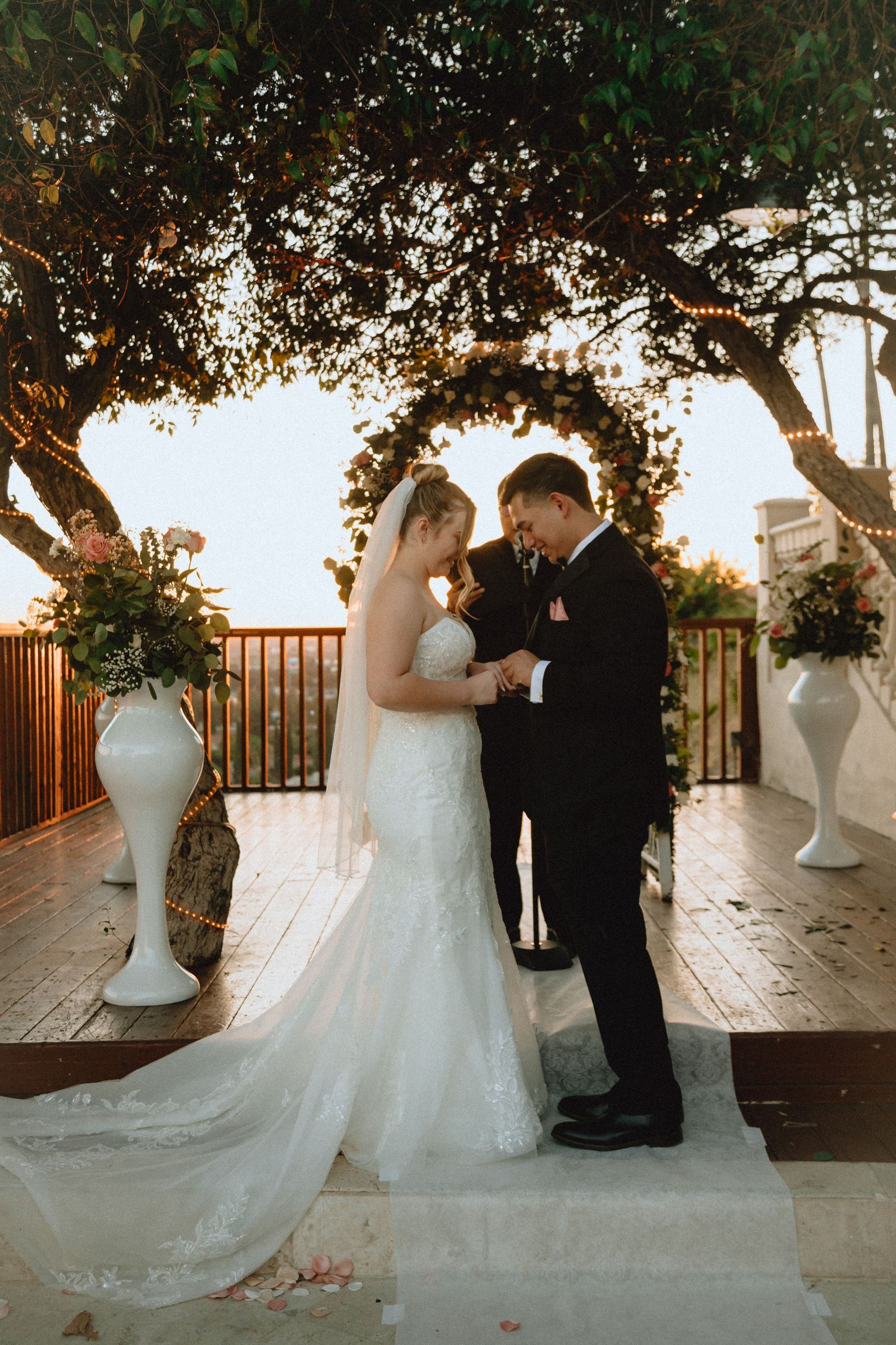 A sunset wedding ceremony with white floral arrangements and twinkle lights decorating the outdoor venue.