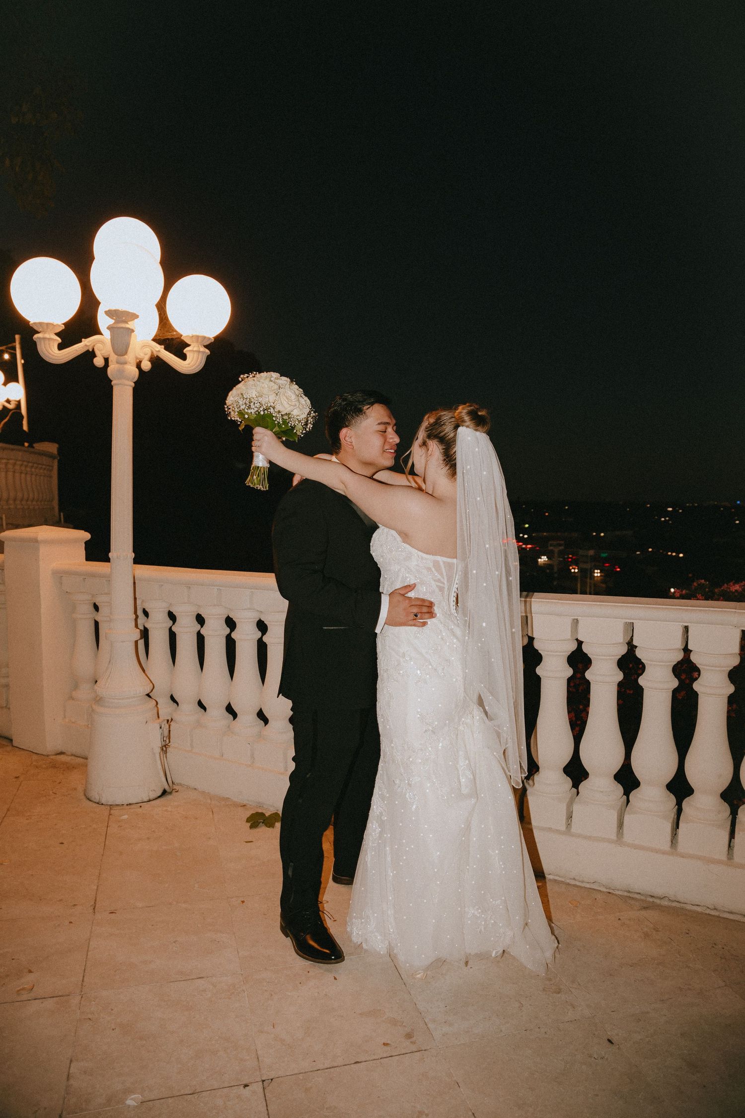 A romantic wedding dance moment captured on a lit balcony with ornate railings.