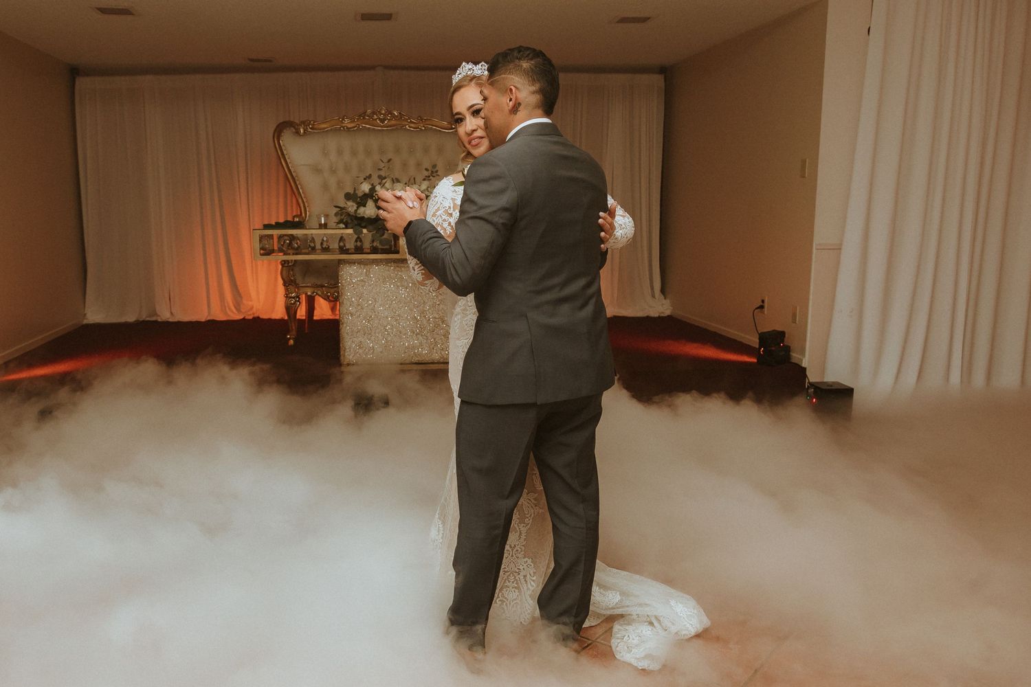 Romantic first dance with dramatic fog effects and warm lighting at wedding reception.