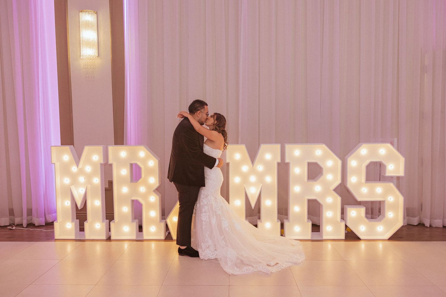 Intimate dance moment captured in front of glowing MR & MRS marquee letters.