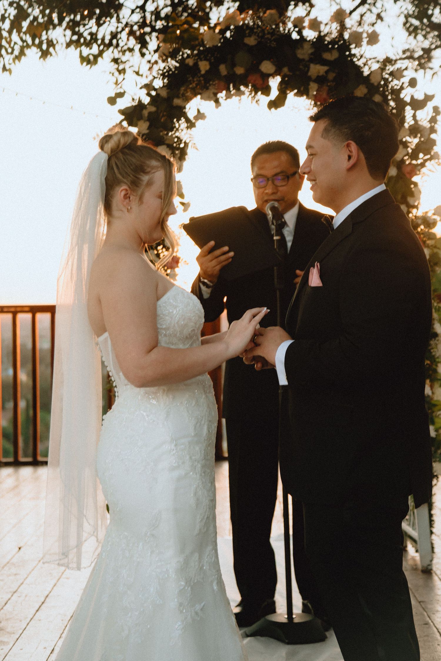 Outdoor wedding ceremony with couple exchanging vows under a leaf-covered arch.
