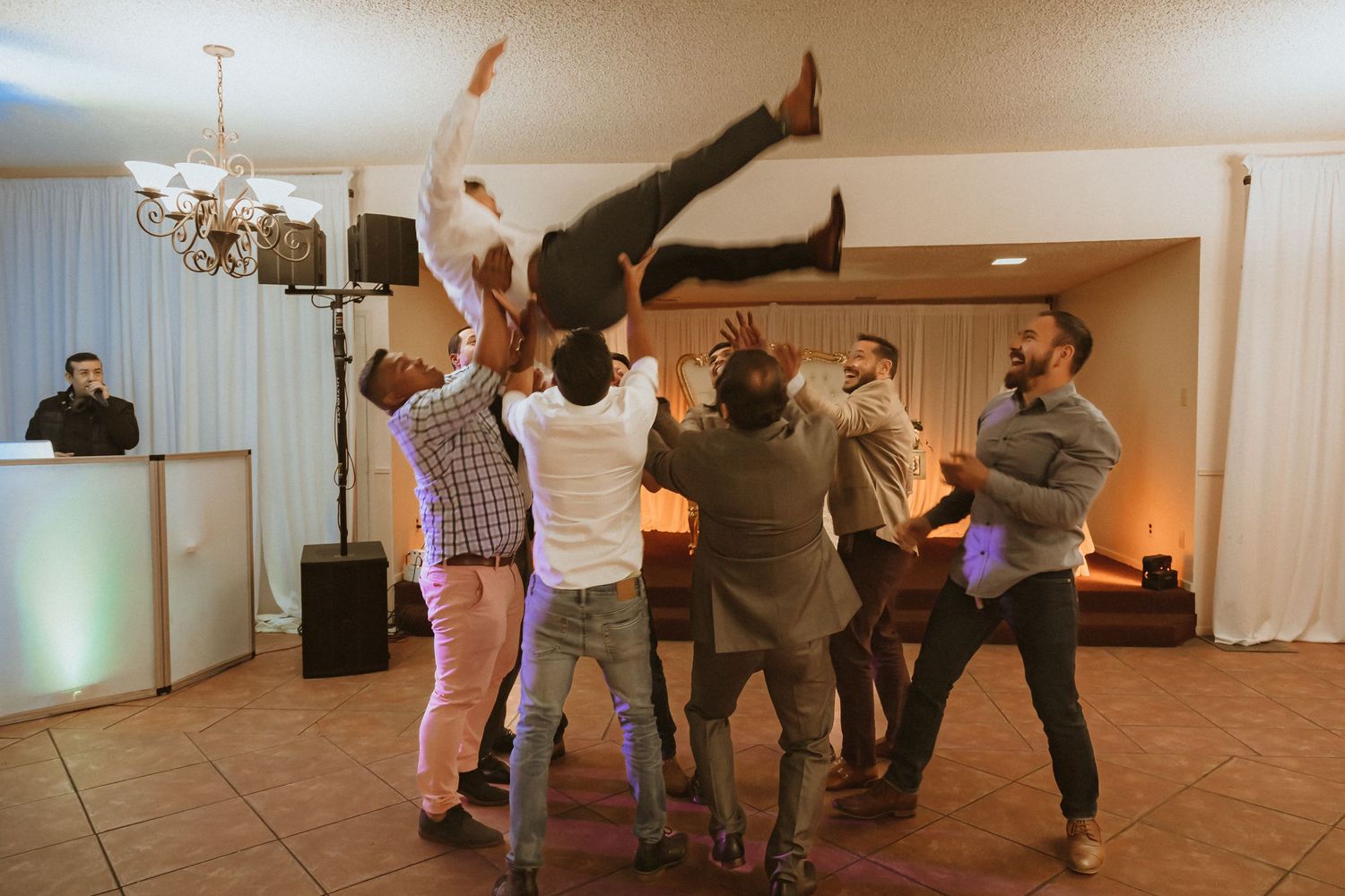 Wedding guests toss a person high in the air during an energetic party celebration.