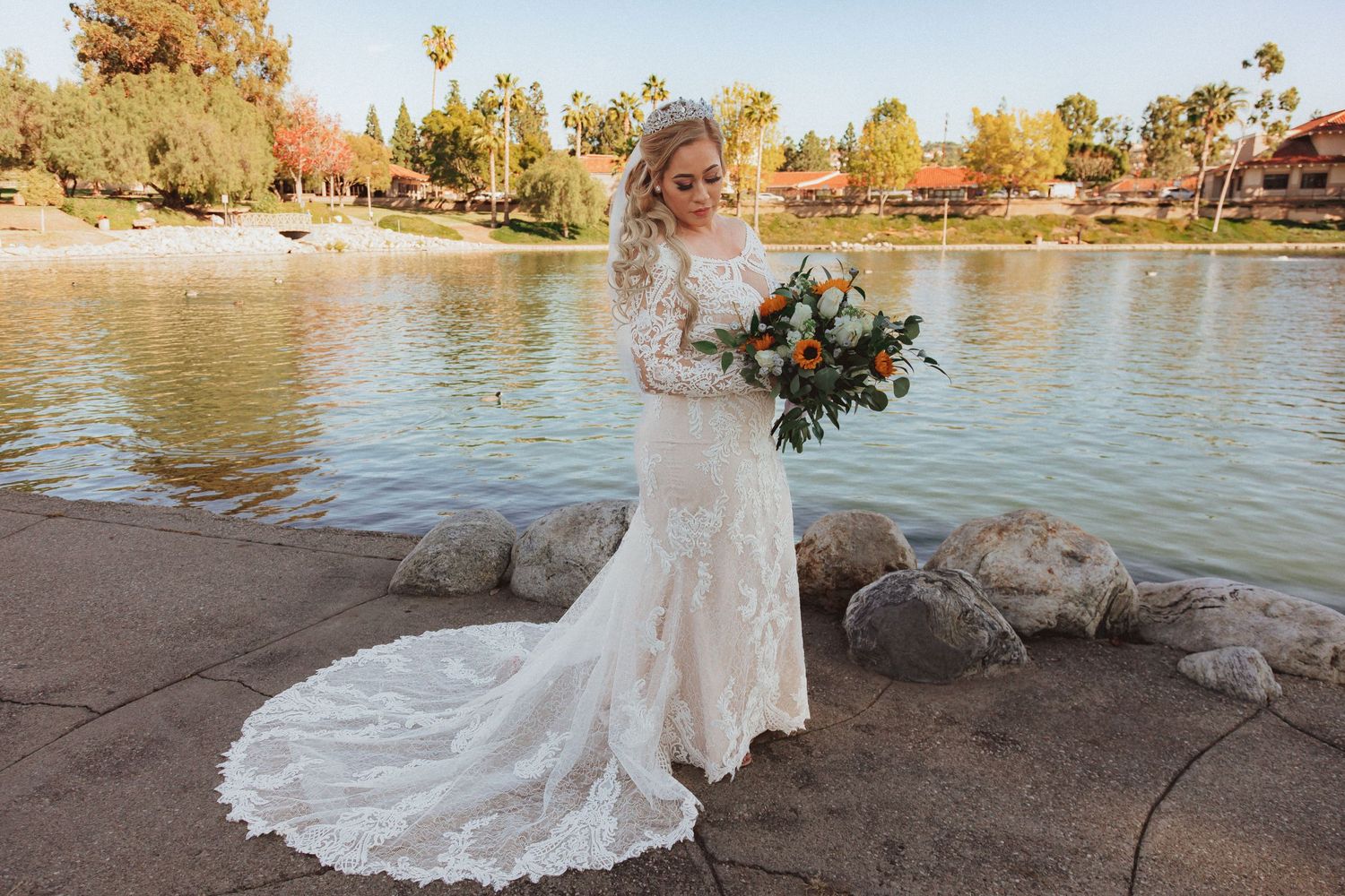 Elegant bridal portrait showing flowing lace train against waterfront backdrop.