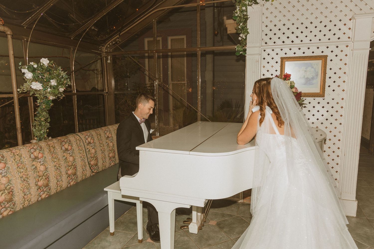 Wedding couple shares an intimate moment near a white piano in a rustic indoor venue.