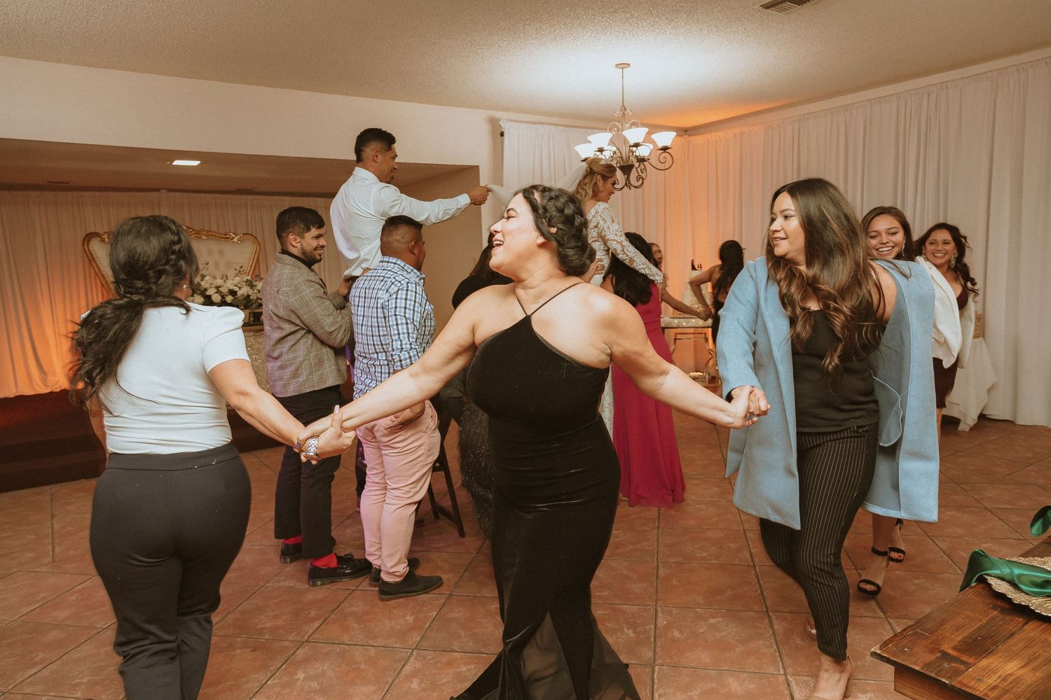 Party guests enjoying synchronized dancing in an indoor venue with warm lighting and tile floors.