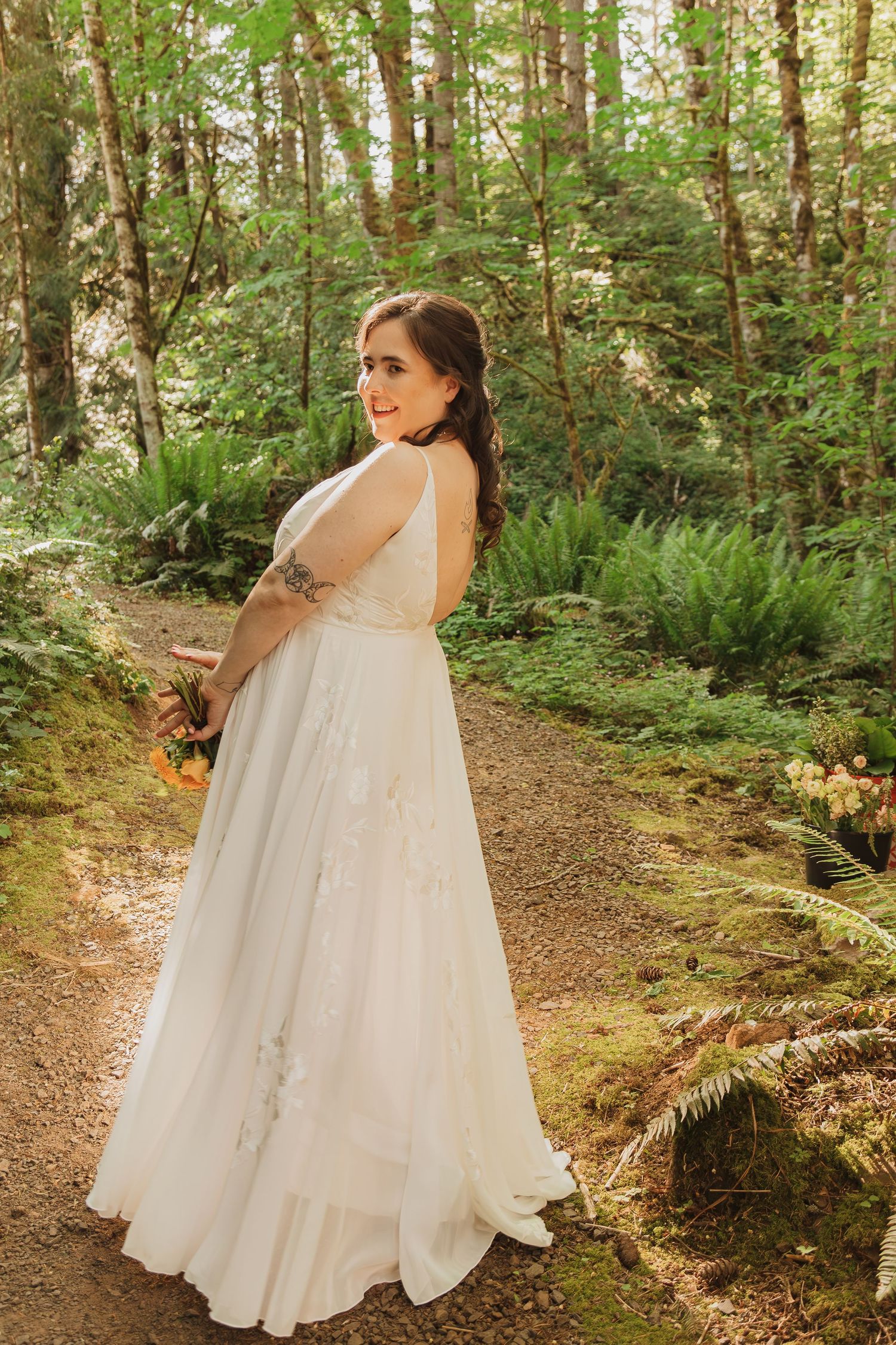 A flowing white wedding dress is showcased on a forest path surrounded by lush greenery.
