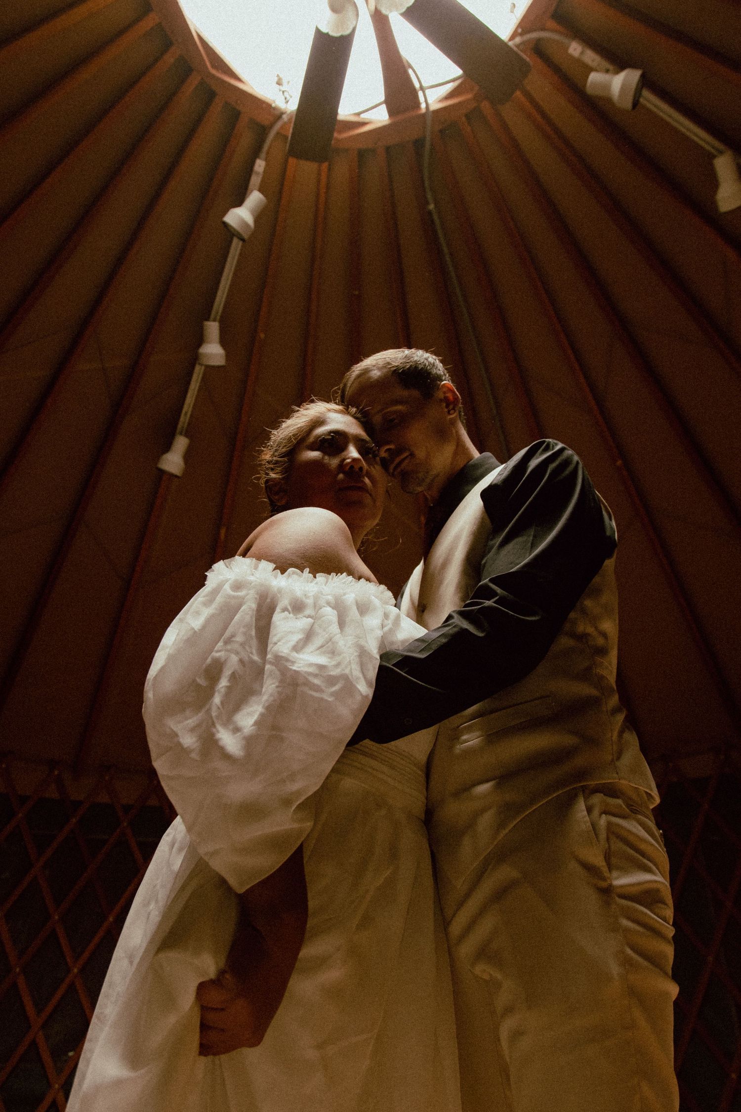 A couple shares an intimate moment under wooden beams in warm, dramatic lighting.