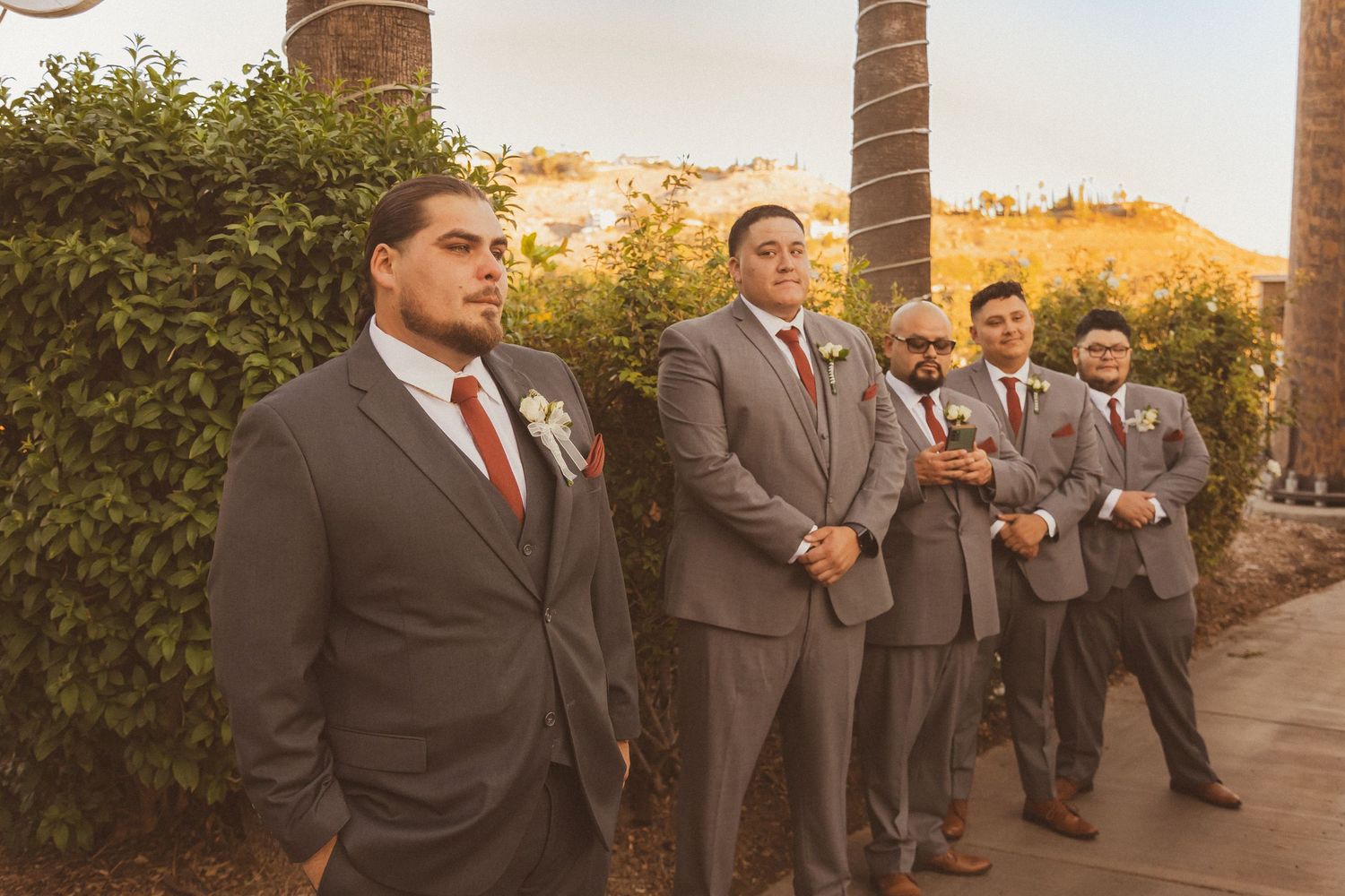 Wedding party in formal attire standing against sunset-lit garden backdrop.