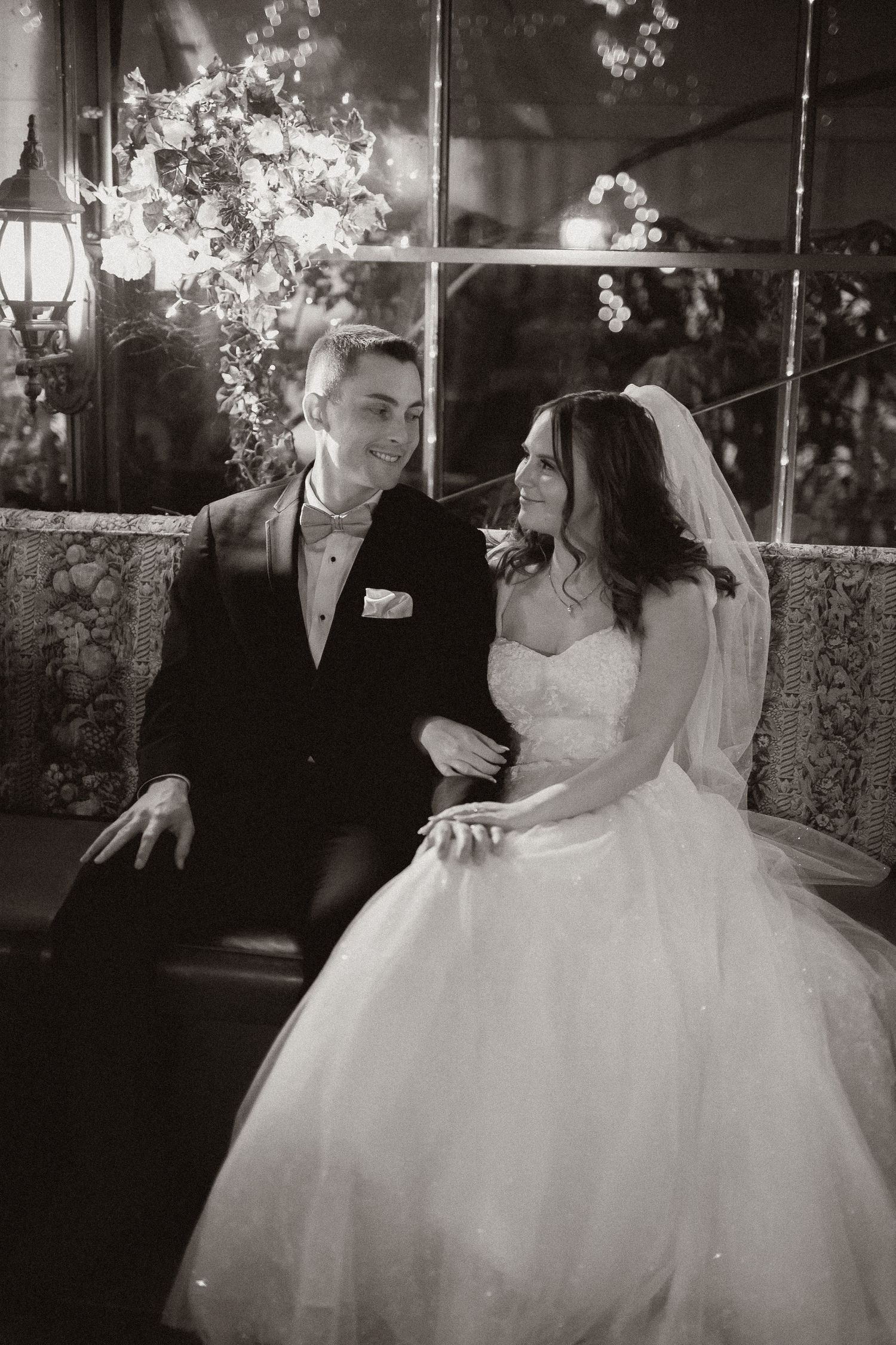 Black and white wedding portrait of newlyweds sitting together under romantic lighting.