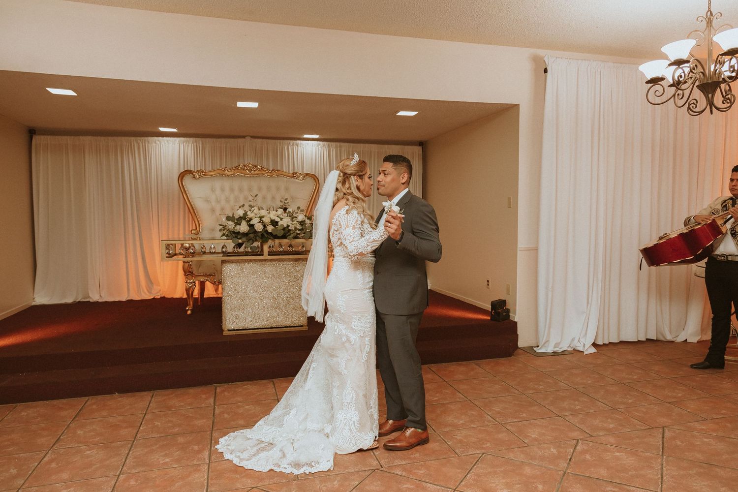 A couple shares their first dance on a tiled floor at their wedding reception.