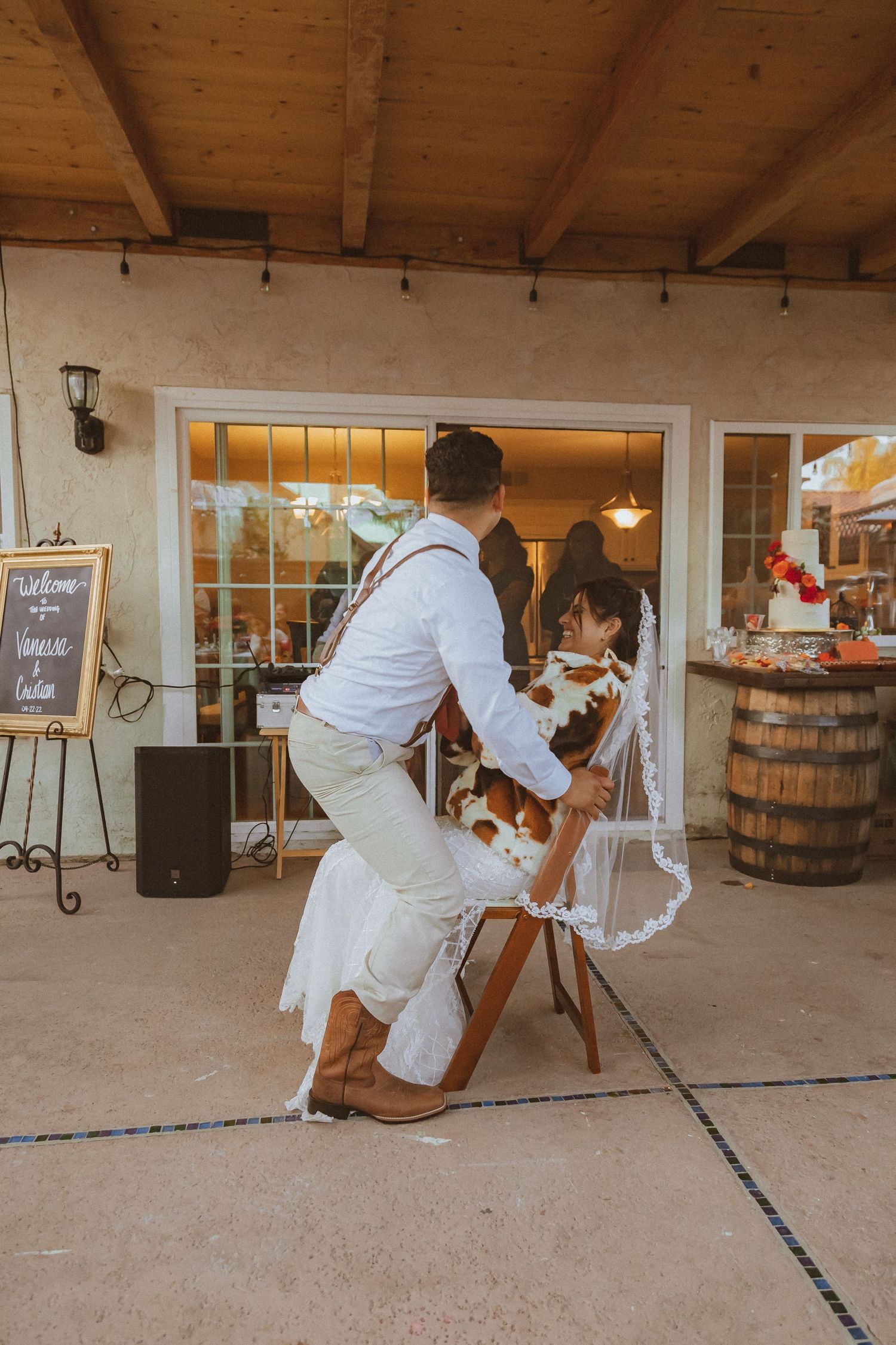 Two people share a fun dance moment on a covered patio with rustic decor and wooden barrels.