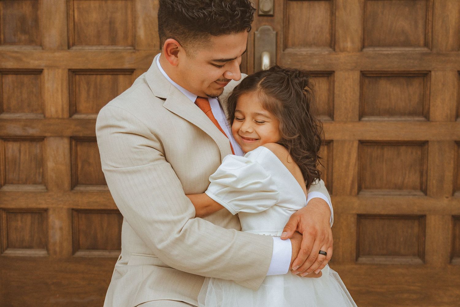 A tender embrace between a couple in wedding attire against a wooden door backdrop.