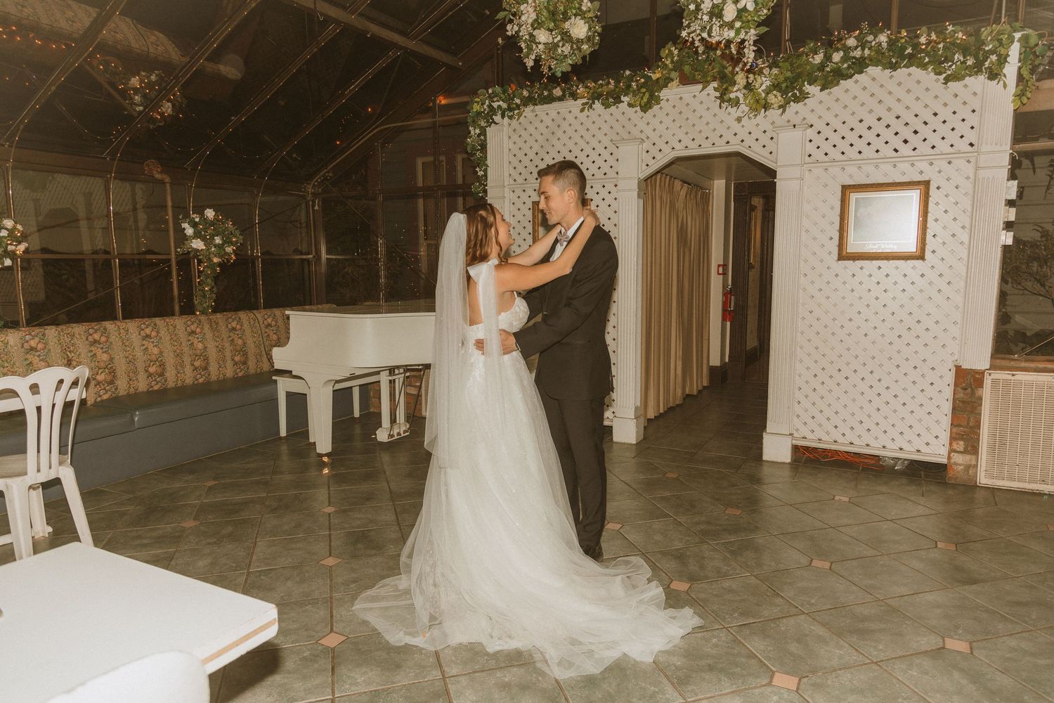 Couple shares first dance in elegant venue with white piano and lattice wall decor.