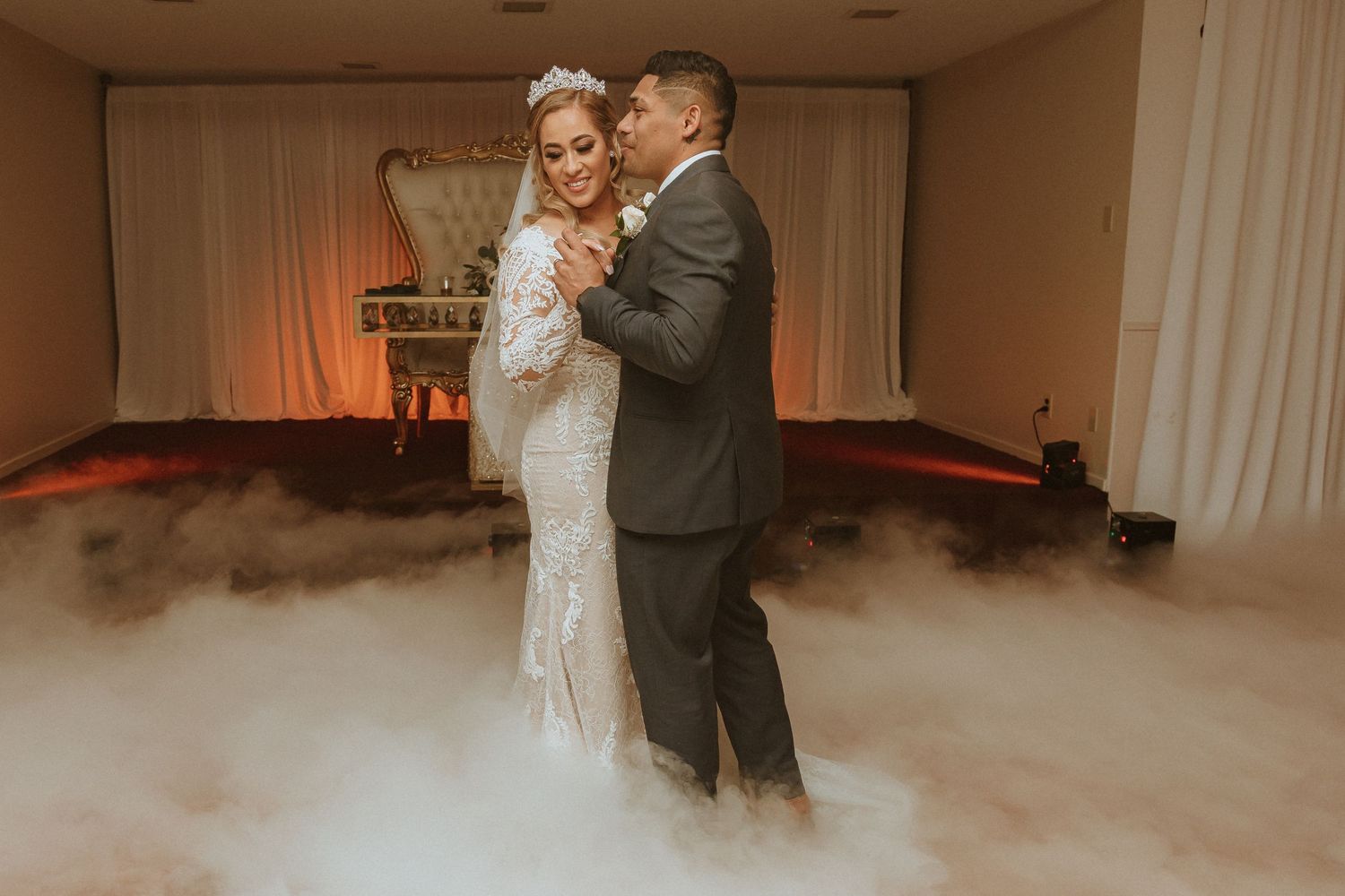 Newlyweds share their first dance surrounded by fog on a dance floor.