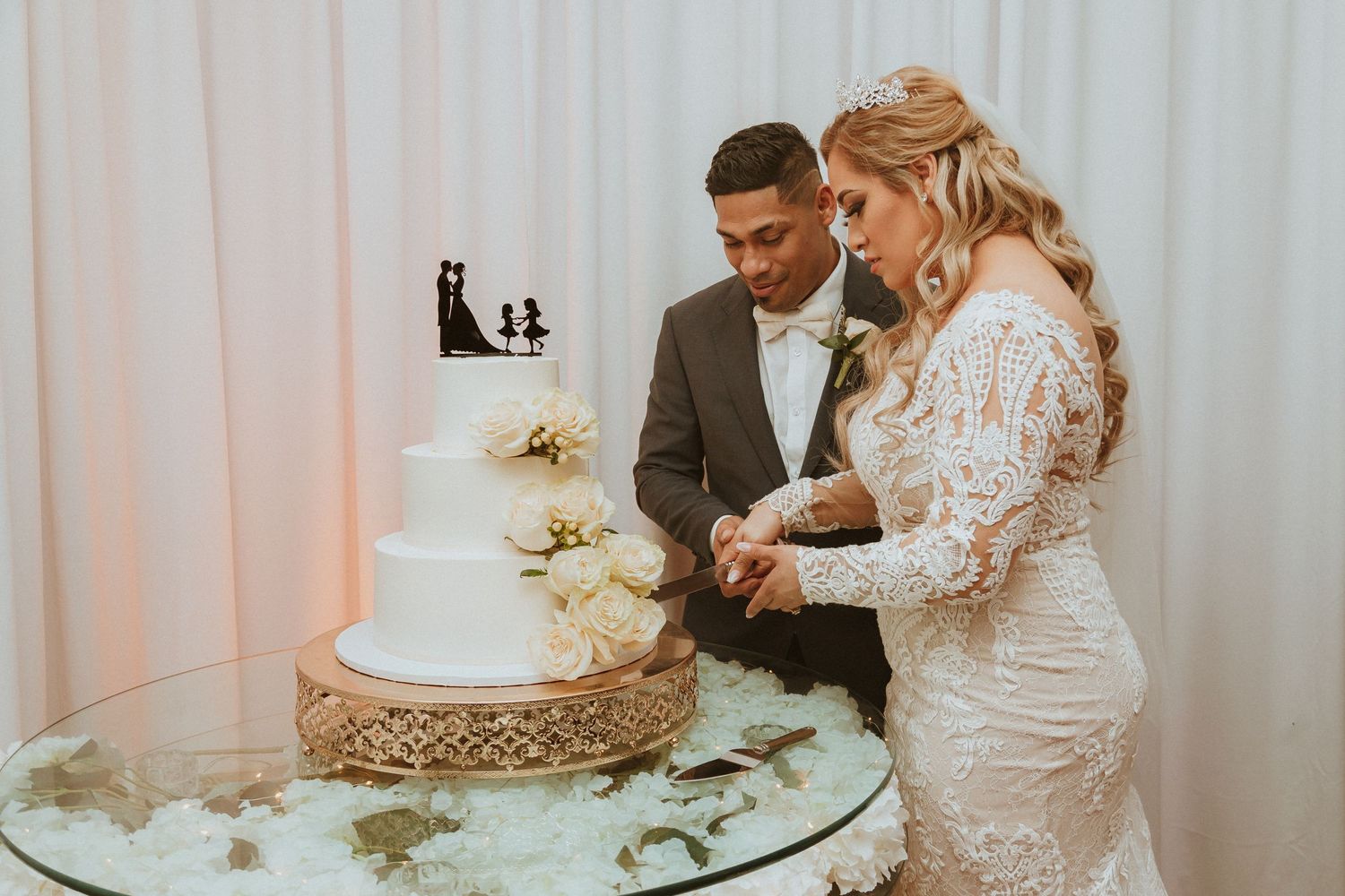 Elegant white tiered wedding cake being cut by couple at reception.