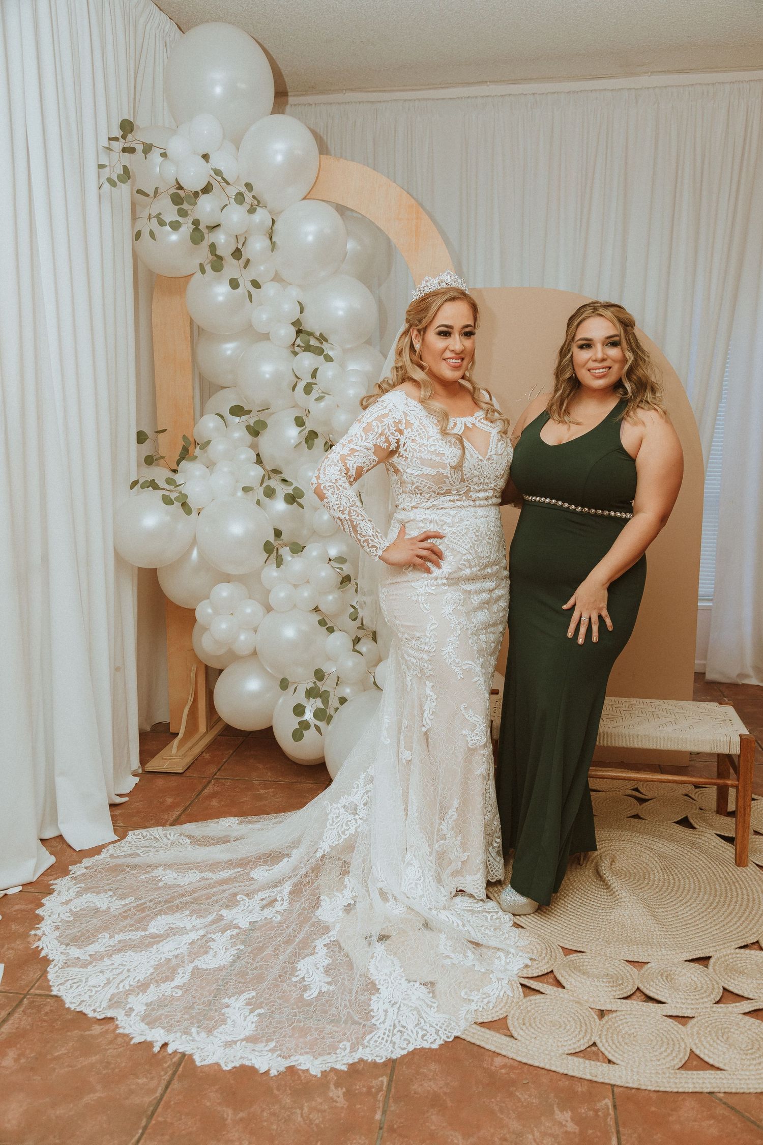 Formal portrait with long lace wedding gown and dark evening dress against white balloon arch.