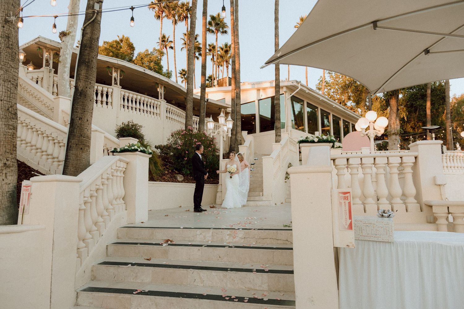 Outdoor wedding venue steps decorated with string lights and white railings at sunset.