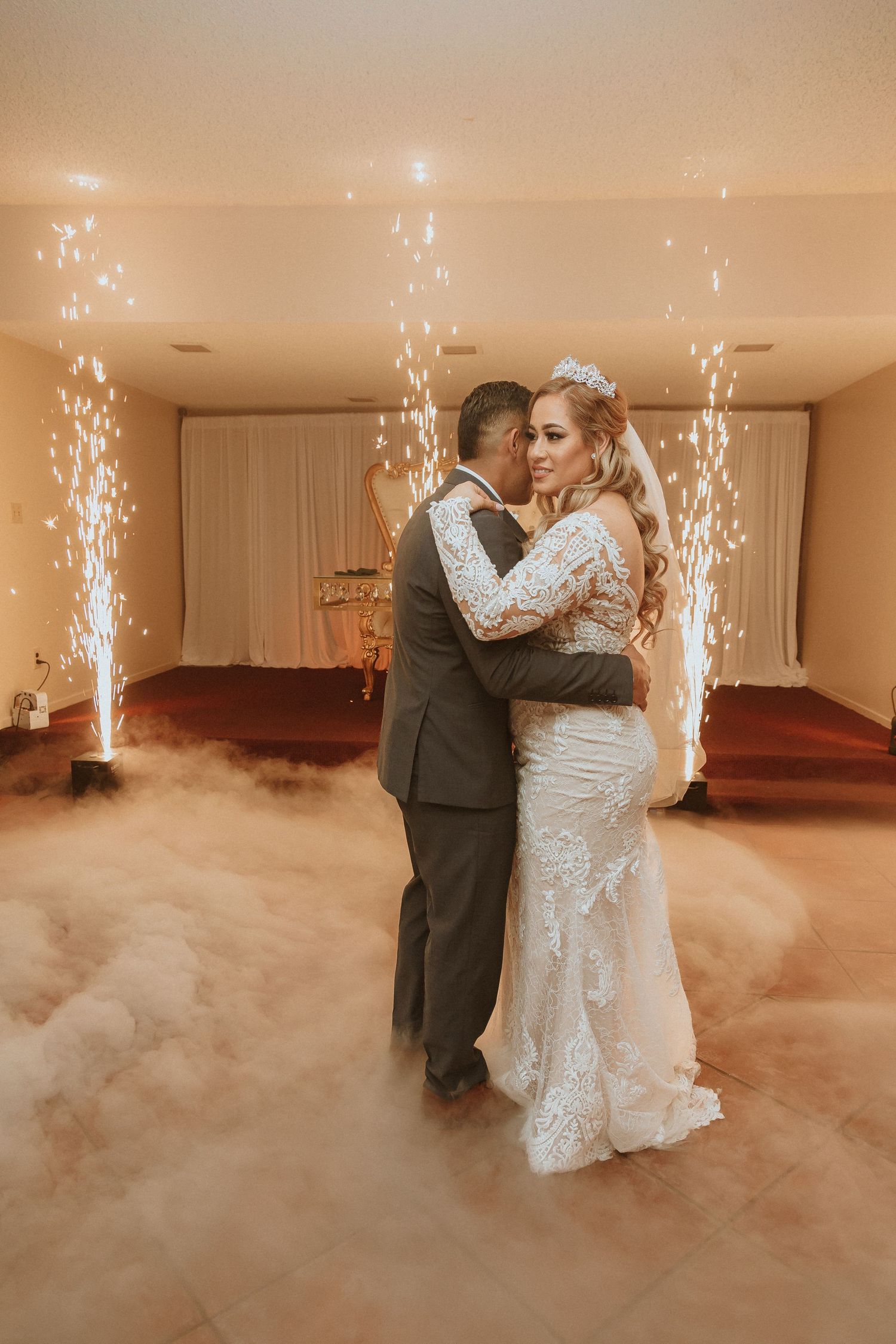 Wedding couple embraces during their first dance with sparkler fountains and dramatic fog effects.