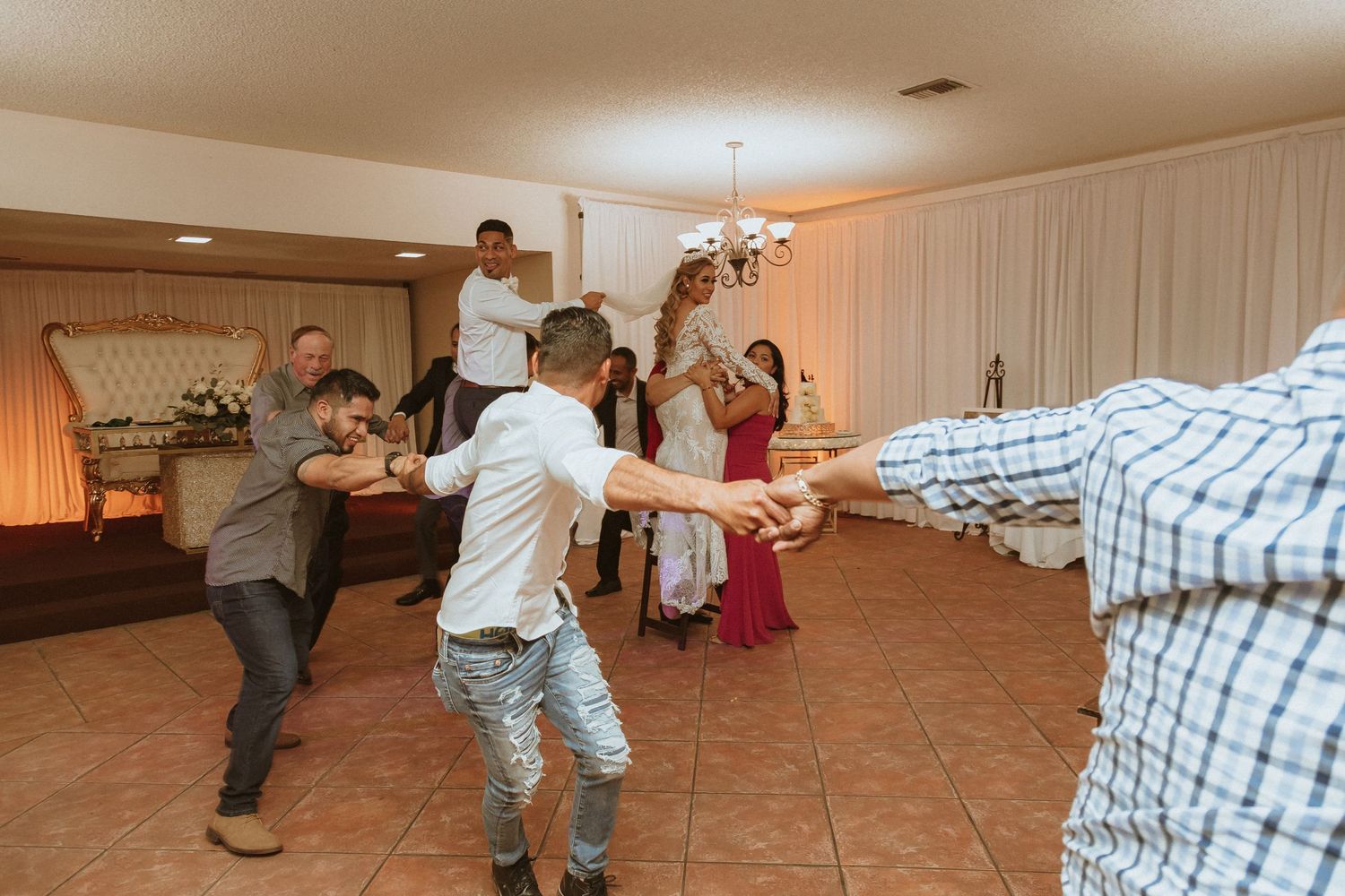 Group of party guests dancing in formation on a tiled floor at an indoor venue.