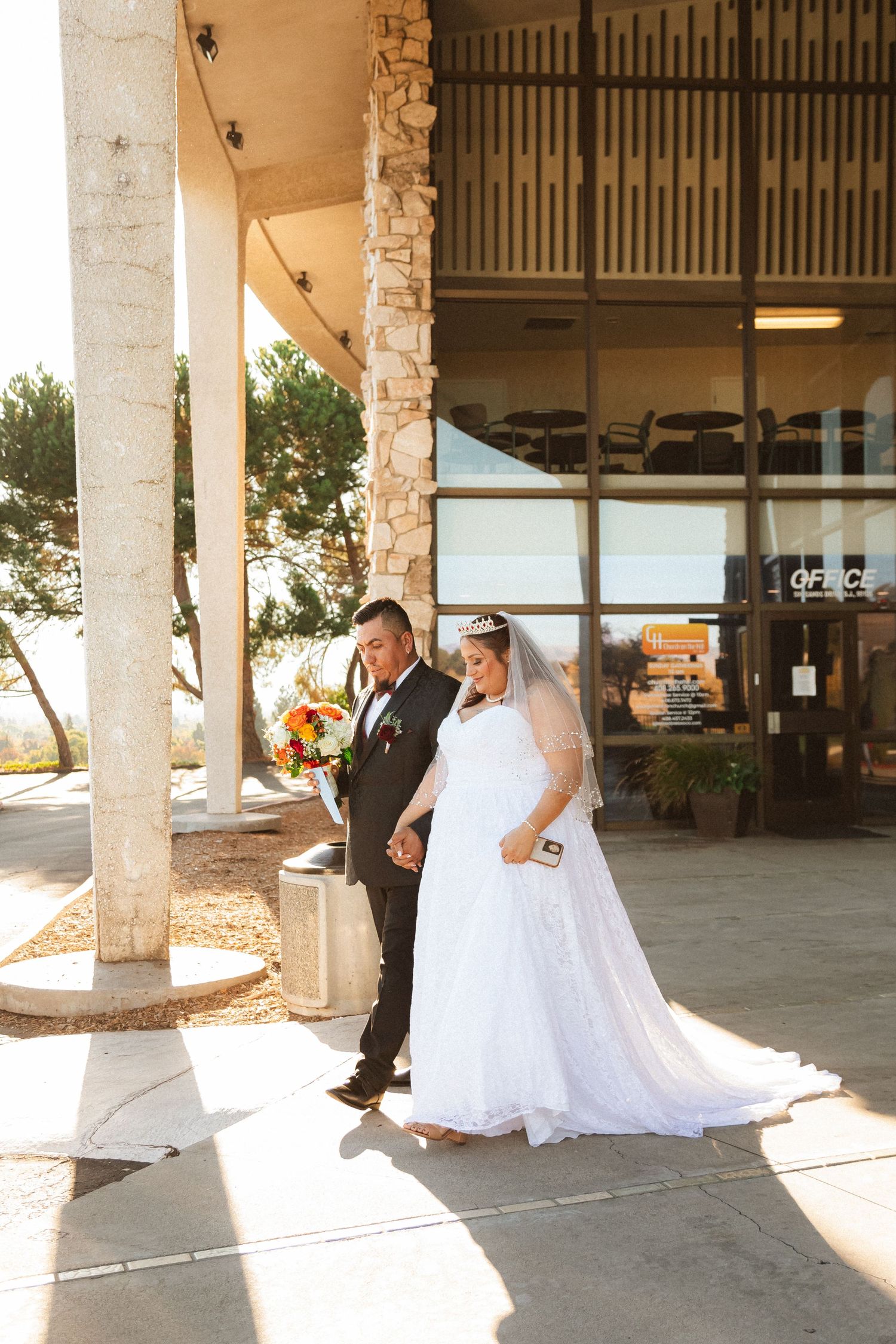 A pair stand together under a covered walkway on their wedding day with natural lighting.