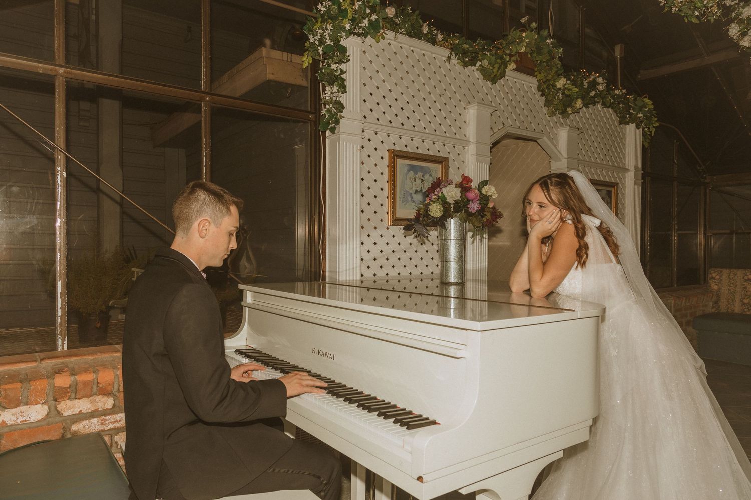 Couple shares an emotional moment at a white grand piano during their wedding celebration.