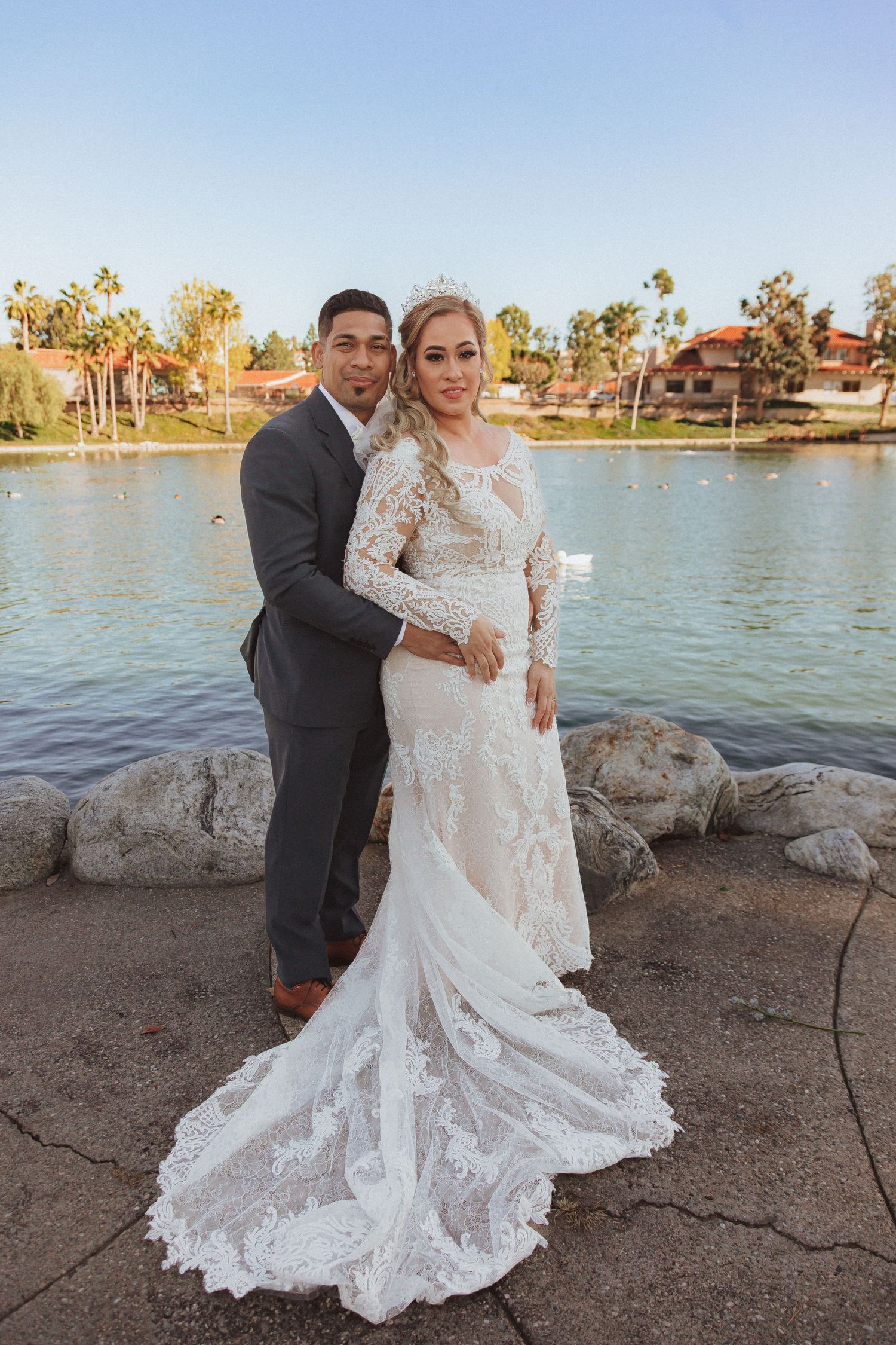 Wedding couple posing against scenic lake backdrop in formal attire.