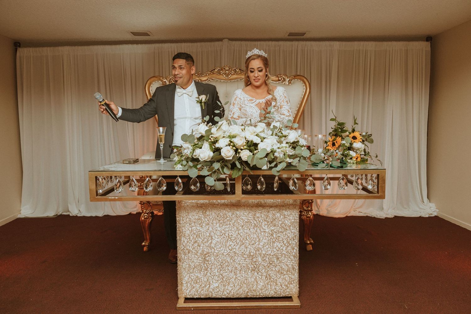 Couple posing playfully behind their elegant wedding reception table with floral centerpieces.