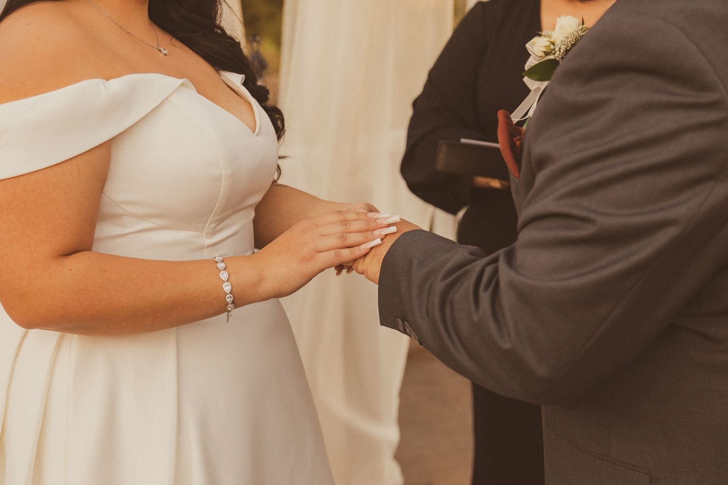 Close-up of ring exchange during wedding ceremony with white dress and dark suit.