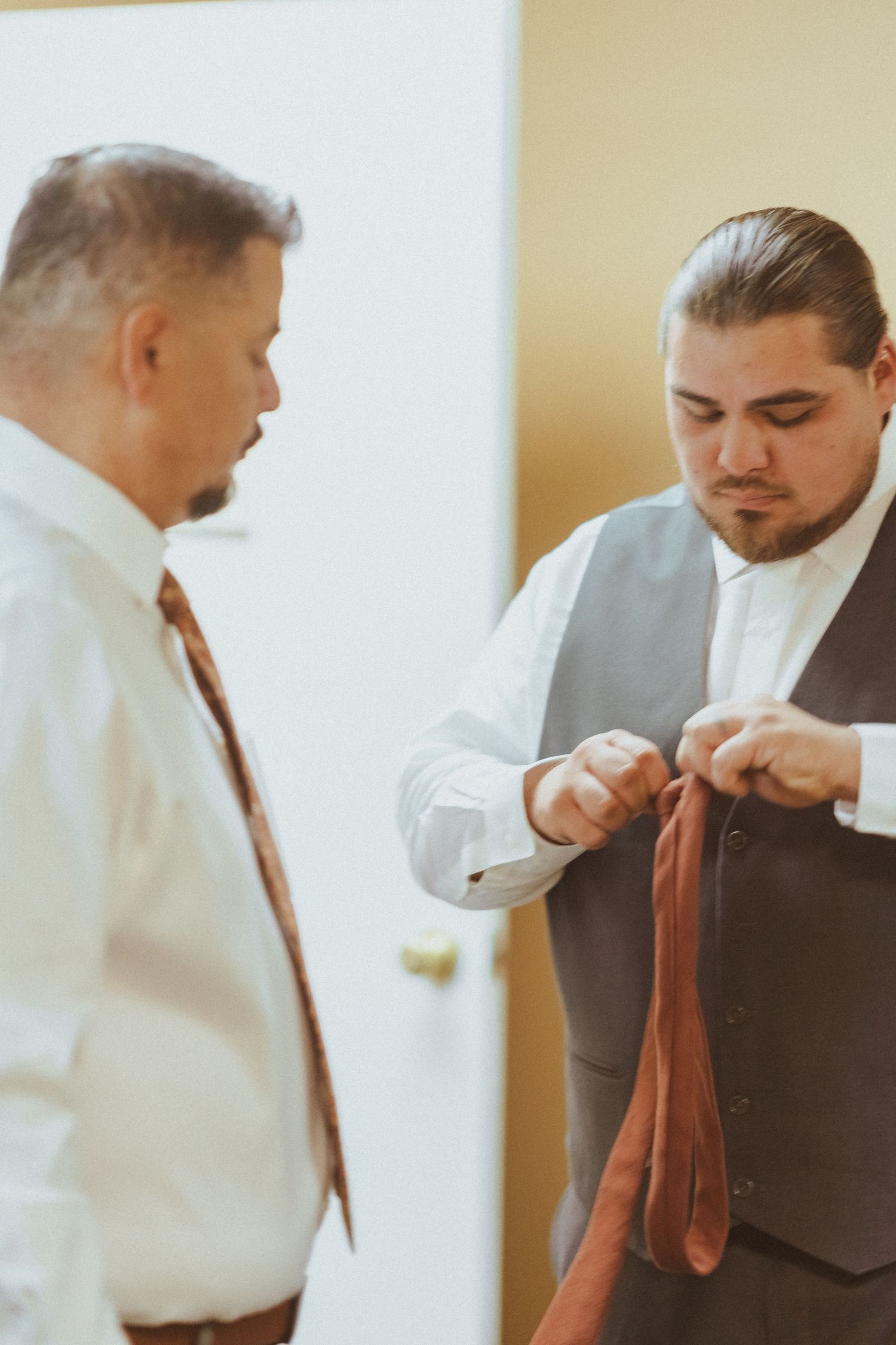 Two people in formal attire preparing for an event, focusing on tie adjustment.