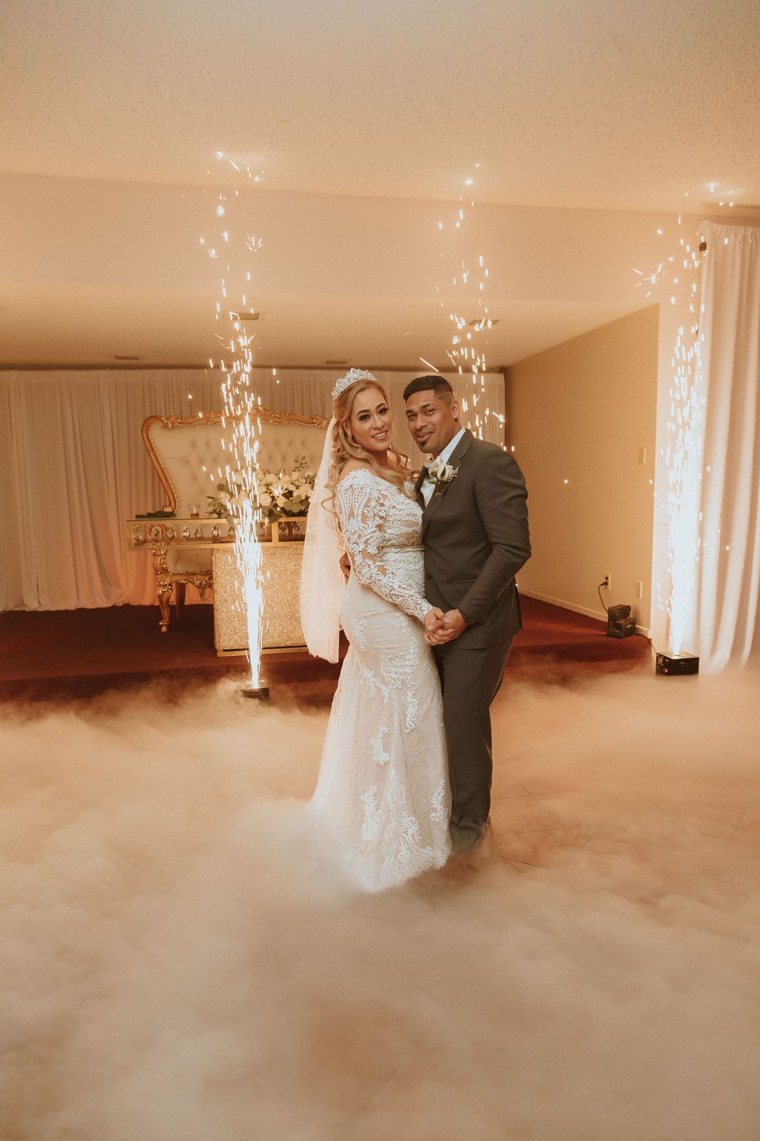 Newlyweds embrace on their wedding day surrounded by low-lying fog and indoor sparkler effects.