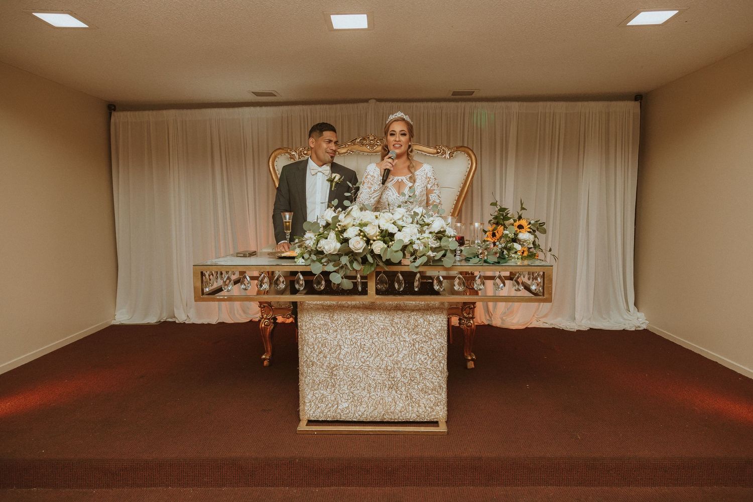 Couple posing behind their wedding reception table adorned with white and peach floral arrangements.
